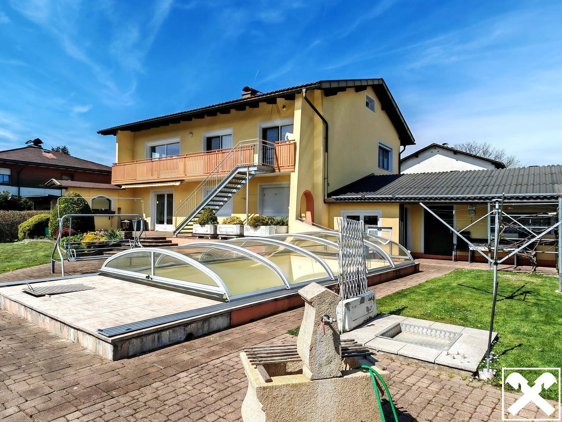 Rückseite des Hauses mit großem Garten, überdachtem Pool und Steinbrunnen.