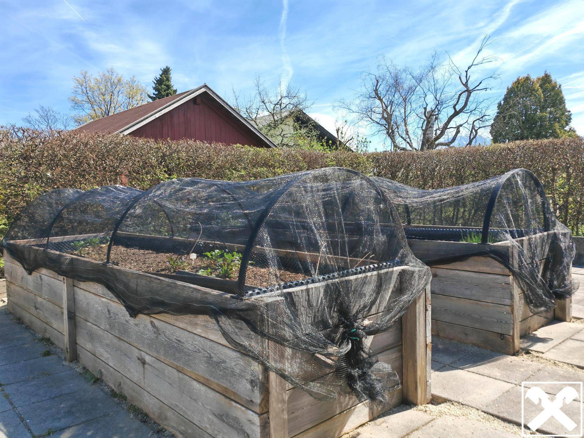 Hochbeete mit Schutznetzen für den Anbau von Gemüse und Kräutern im Garten.