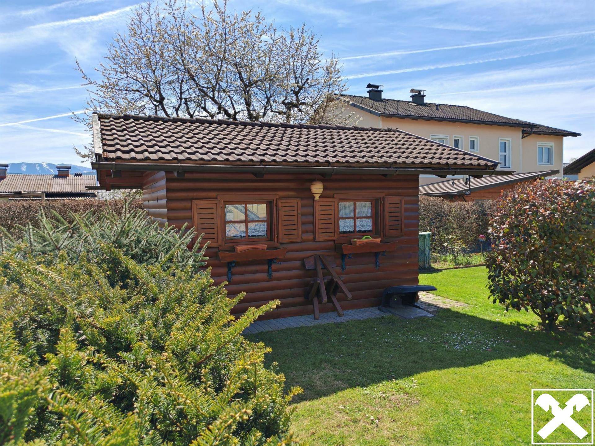Charmantes Holzgartenhaus mit Fenstern und Blumenkästen in gepflegter Gartenanlage.