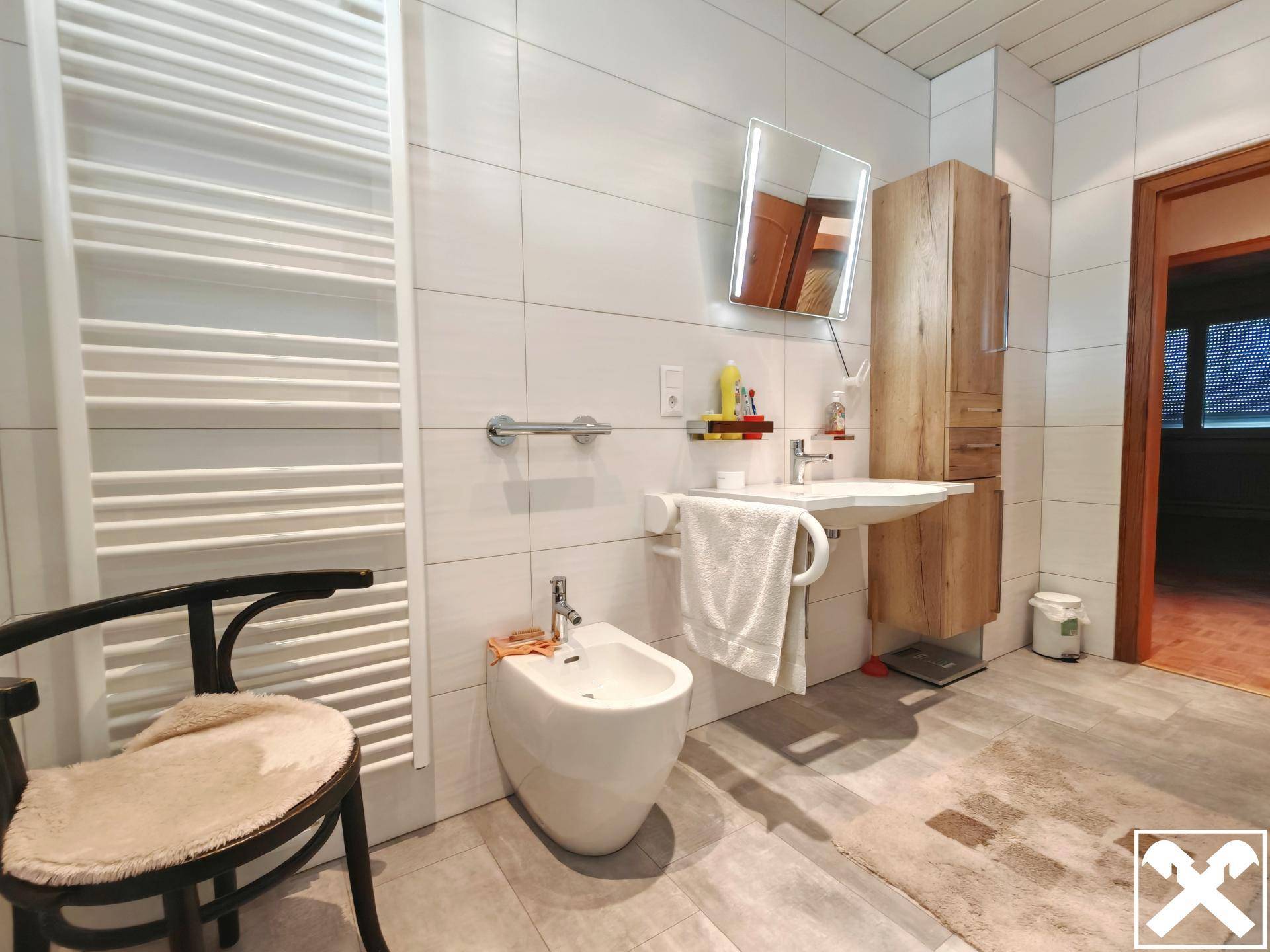 Modernes Badezimmer mit weißen Fliesen, Bidet, wandmontiertem WC und Handtuchheizkörper.