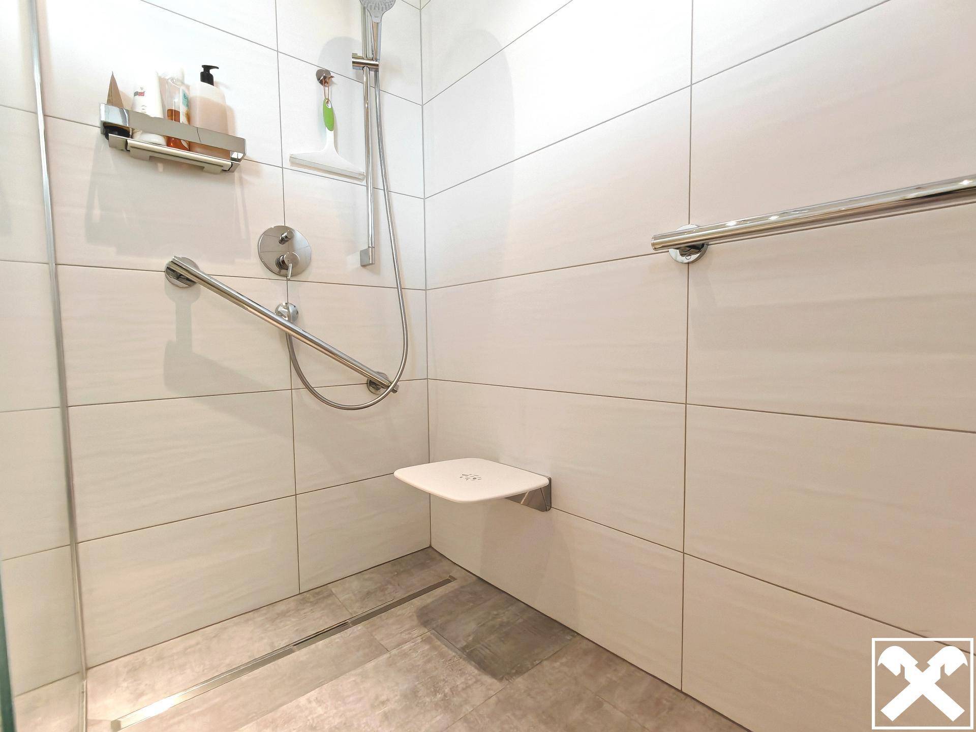 Barrierefreie Dusche mit Haltegriffen, Duschsitz und großformatigen Fliesen.