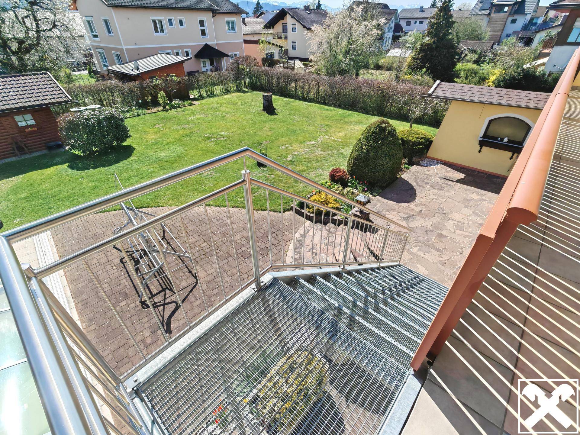 Außentreppe aus Metall führt vom Balkon hinunter zum gepflasterten Gartenbereich.