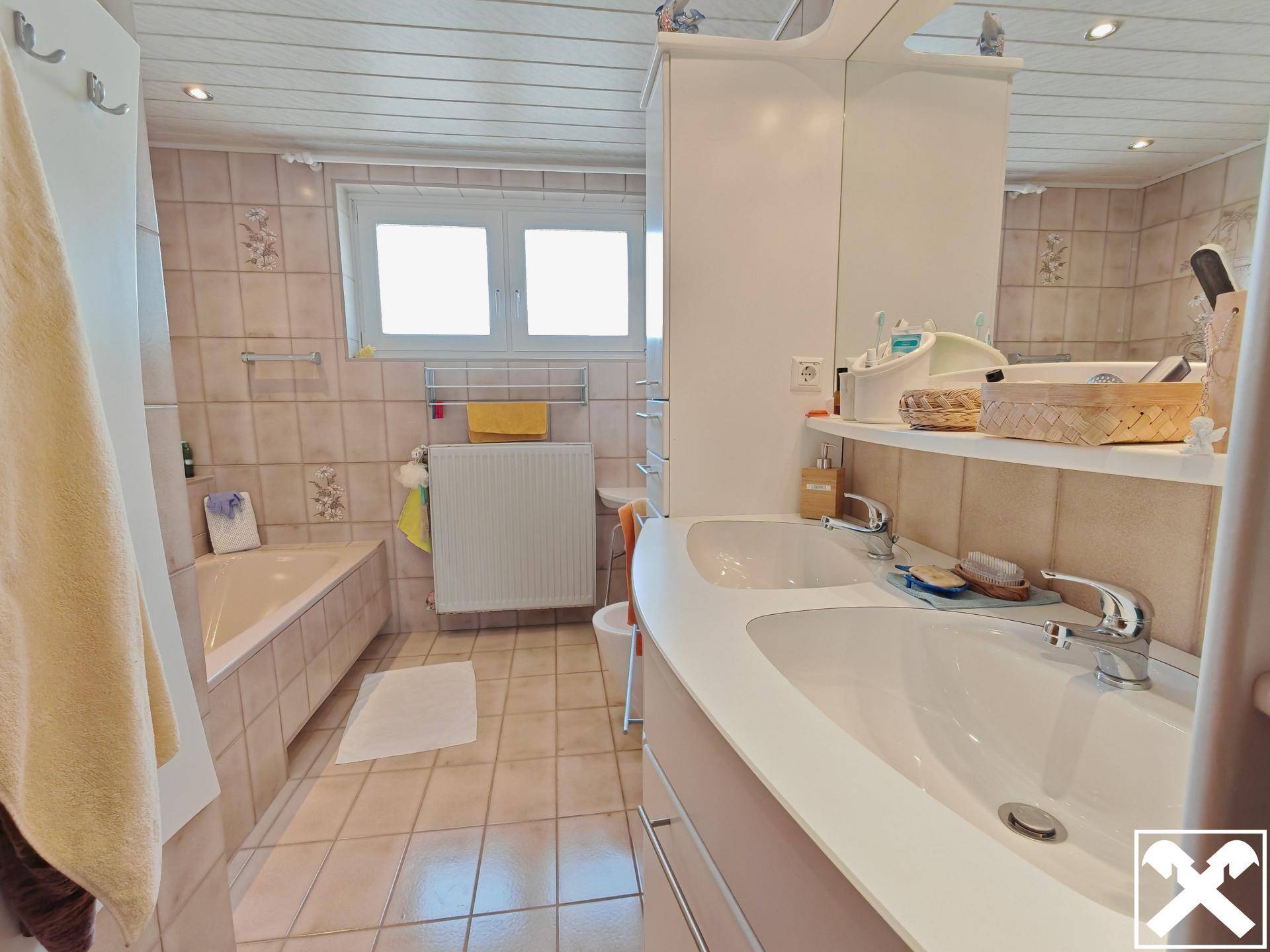 Badezimmer mit Doppelwaschbecken, Badewanne, Fenster und Holzdecke.