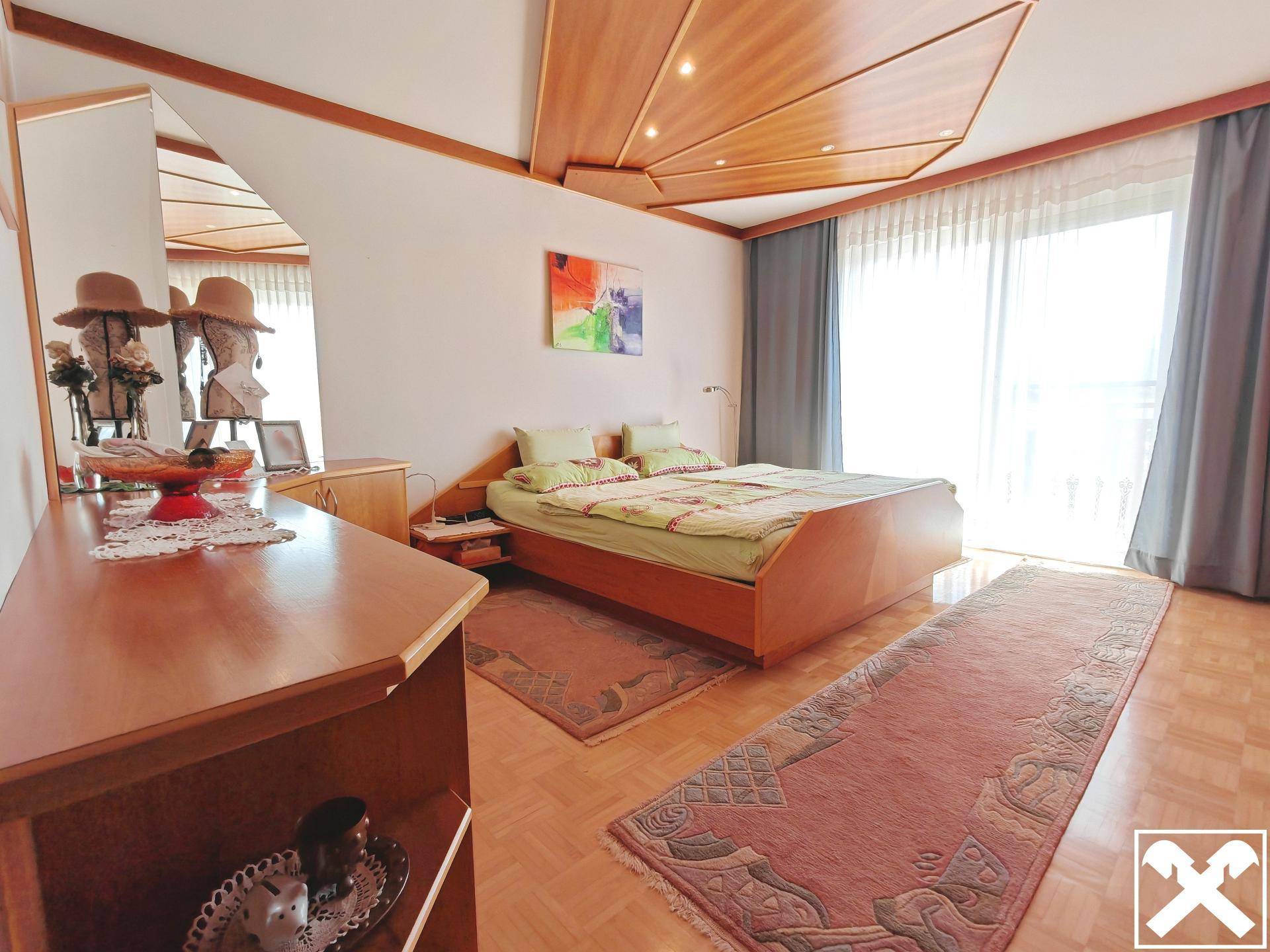 Helles Schlafzimmer mit Holzboden, dekorativer Decke und Zugang zum Balkon.