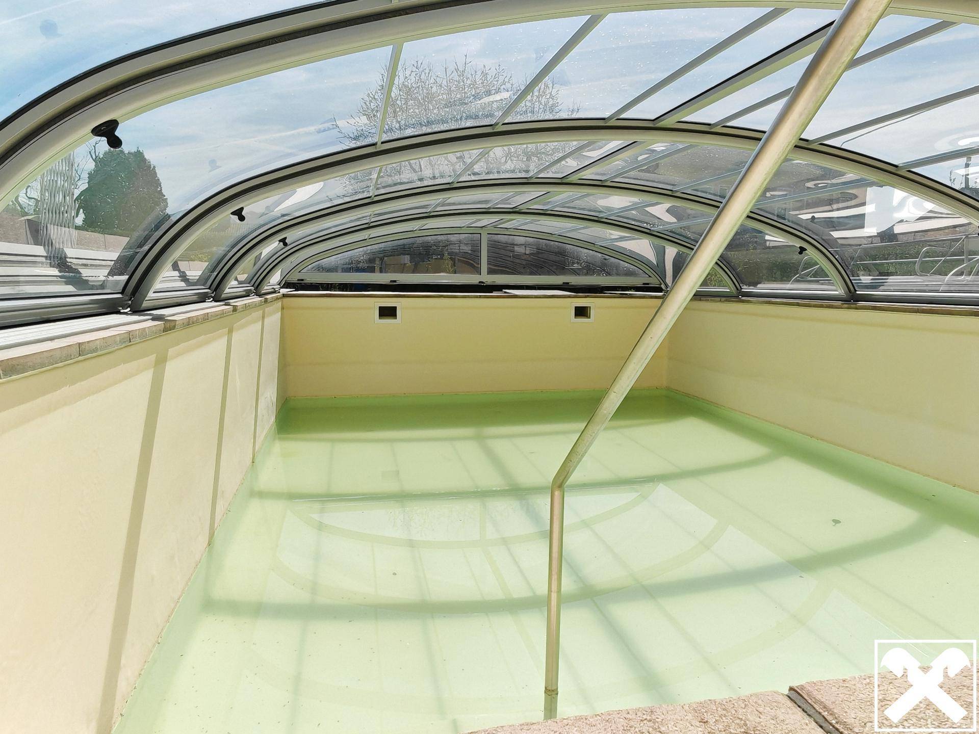 Innenansicht des überdachten Pools mit klarem Wasser und Einstiegsleiter.