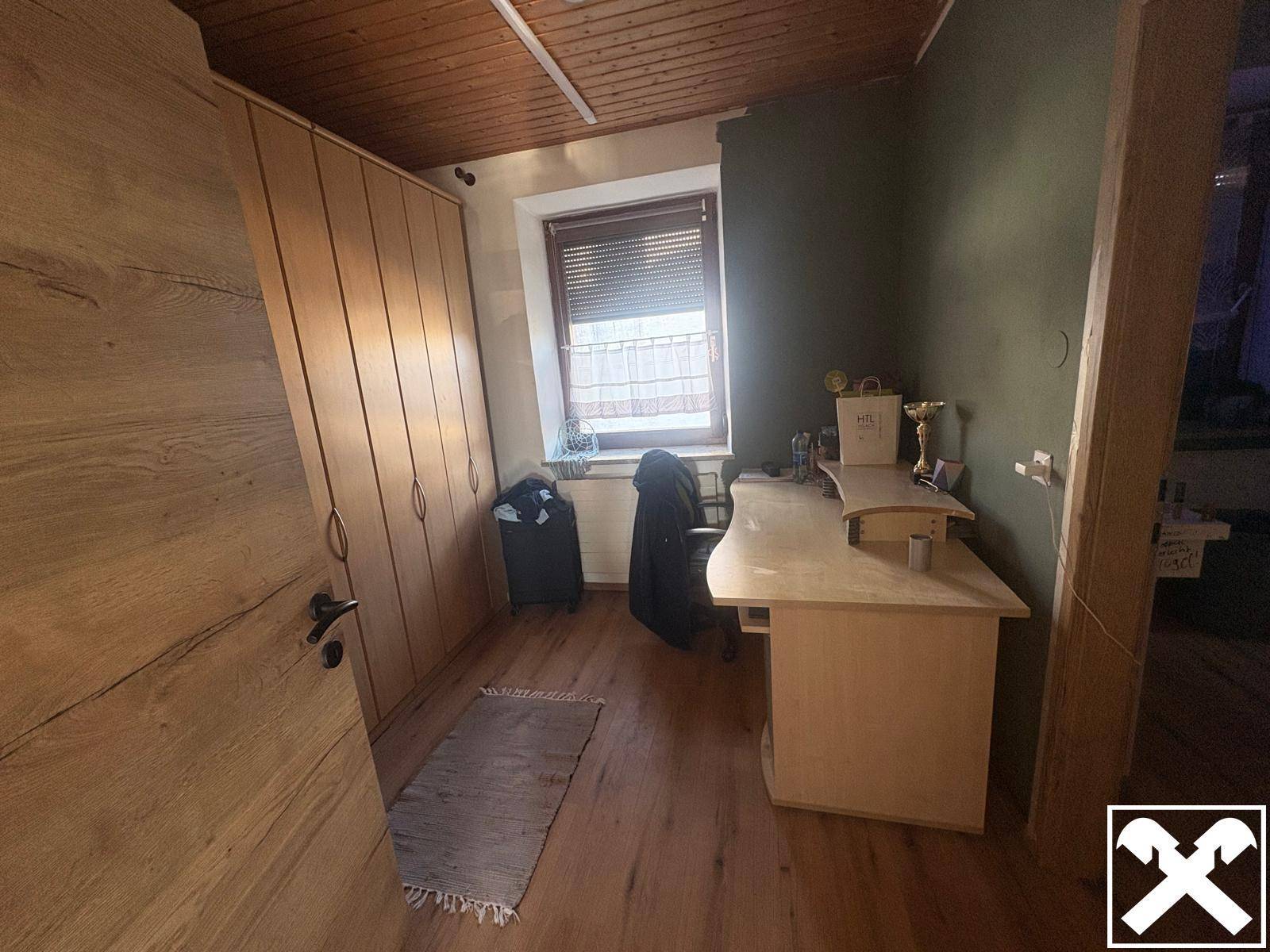 Helles Arbeitszimmer mit Holzdecke, Einbauschränken und Schreibtisch am Fenster.