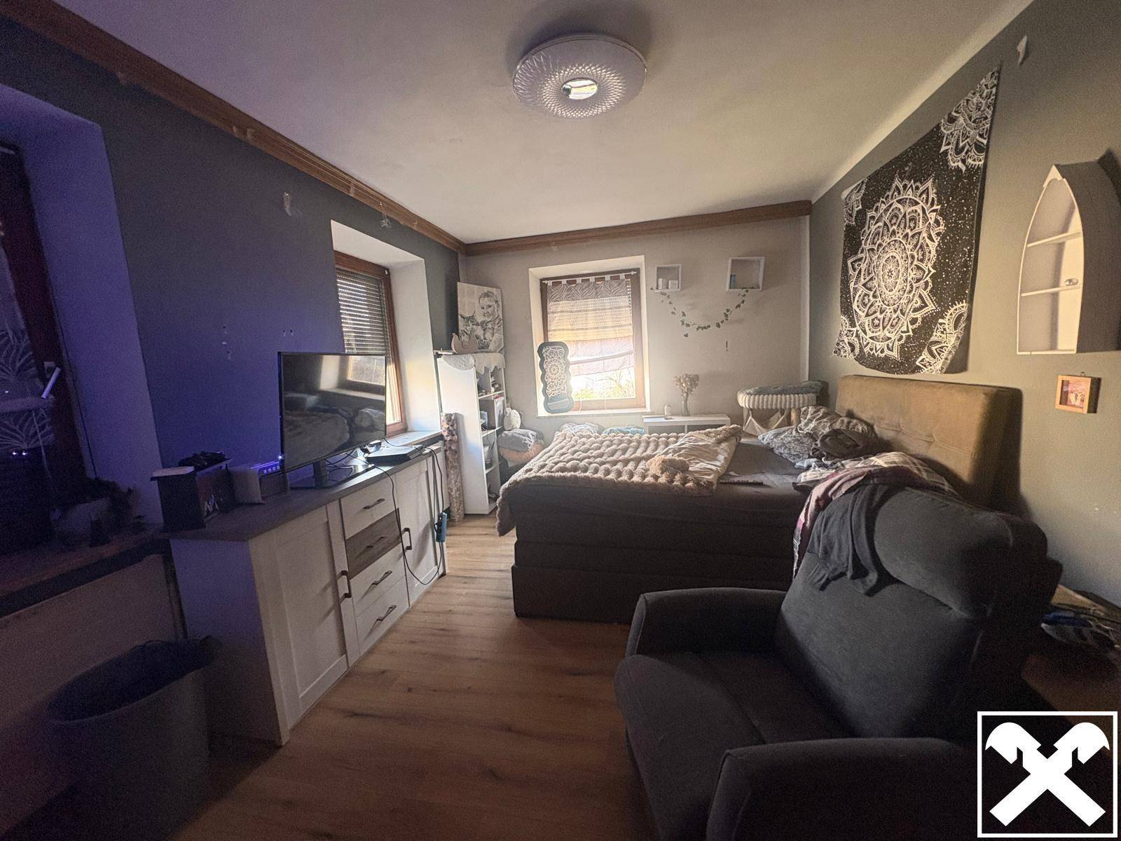 Schlafzimmer mit Holzboden, großem Bett und Fernseher auf einem Sideboard.