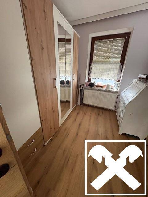 Schlafzimmerbereich mit Spiegelschrank, Holzboden und Fenster mit Rollladen.