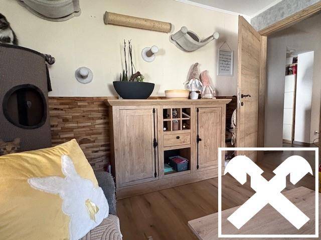 Wohnbereich mit Holzboden, Sideboard und dekorativen Elementen an der Wand.