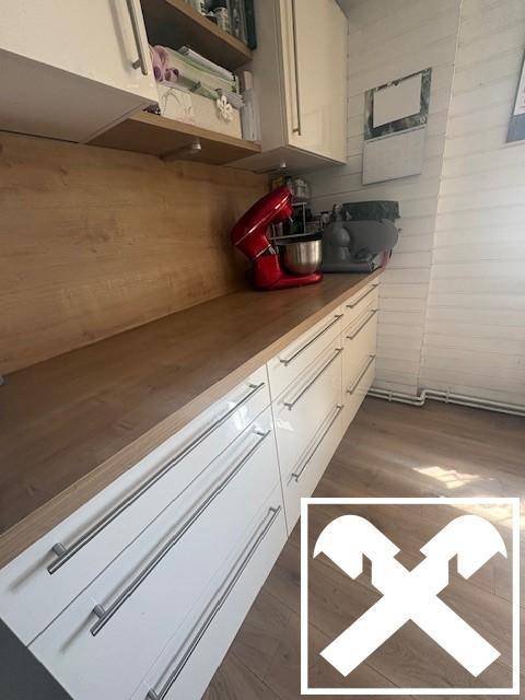 Moderne Küche mit weißen Hochglanzschubladen, Holzarbeitsplatte und Küchengeräten.