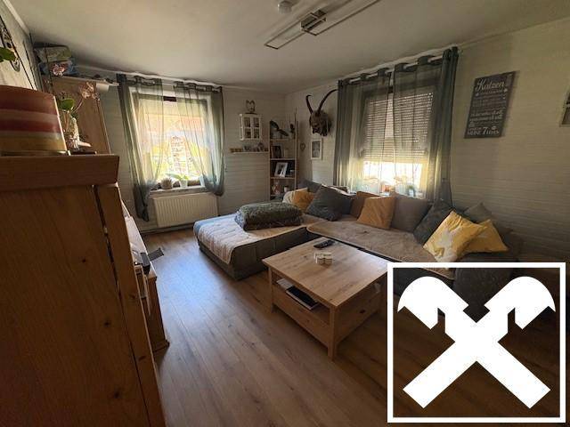 Gemütliches Wohnzimmer mit großem Sofa, Couchtisch und Fenstern mit Blick ins Grüne.