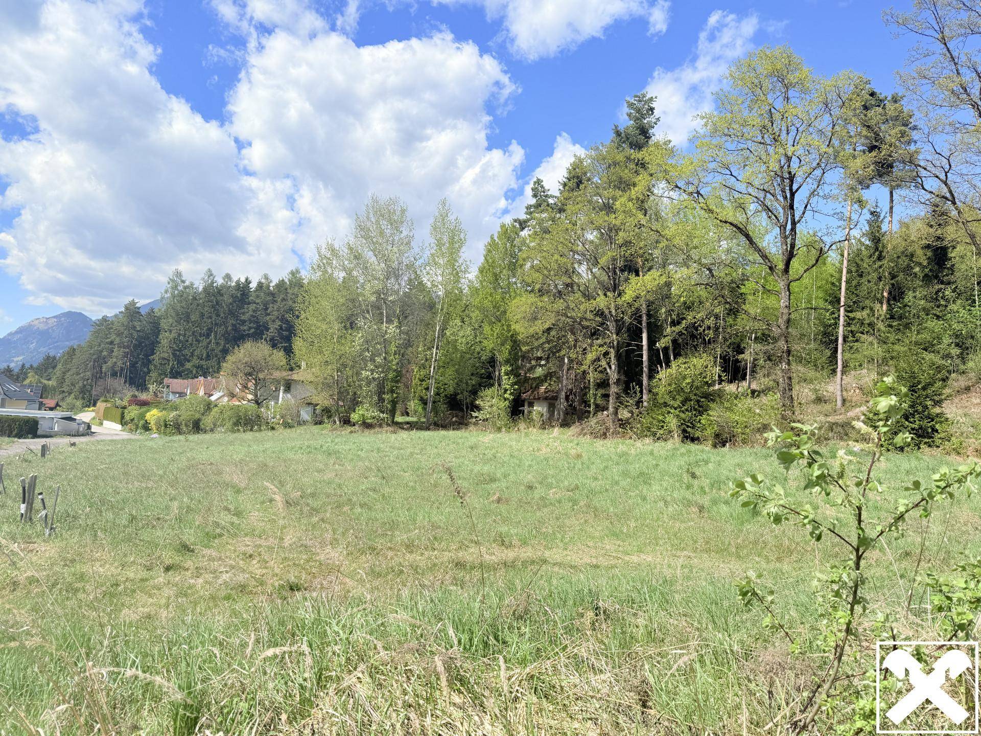 Grüne Wiesen und Bäume mit einem Blick auf entfernte Häuser und die umliegende Natur.