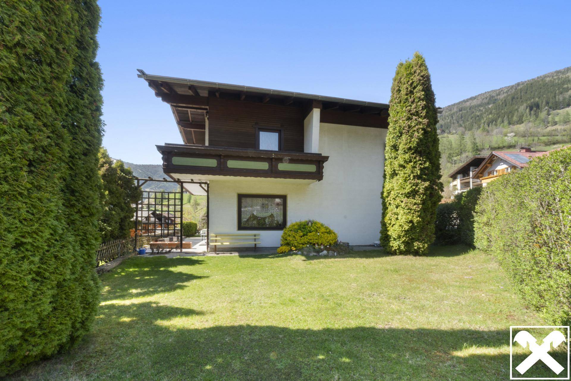 Seitlicher Blick auf das Haus mit gepflegtem Rasen und hohen Hecken im Vordergrund.