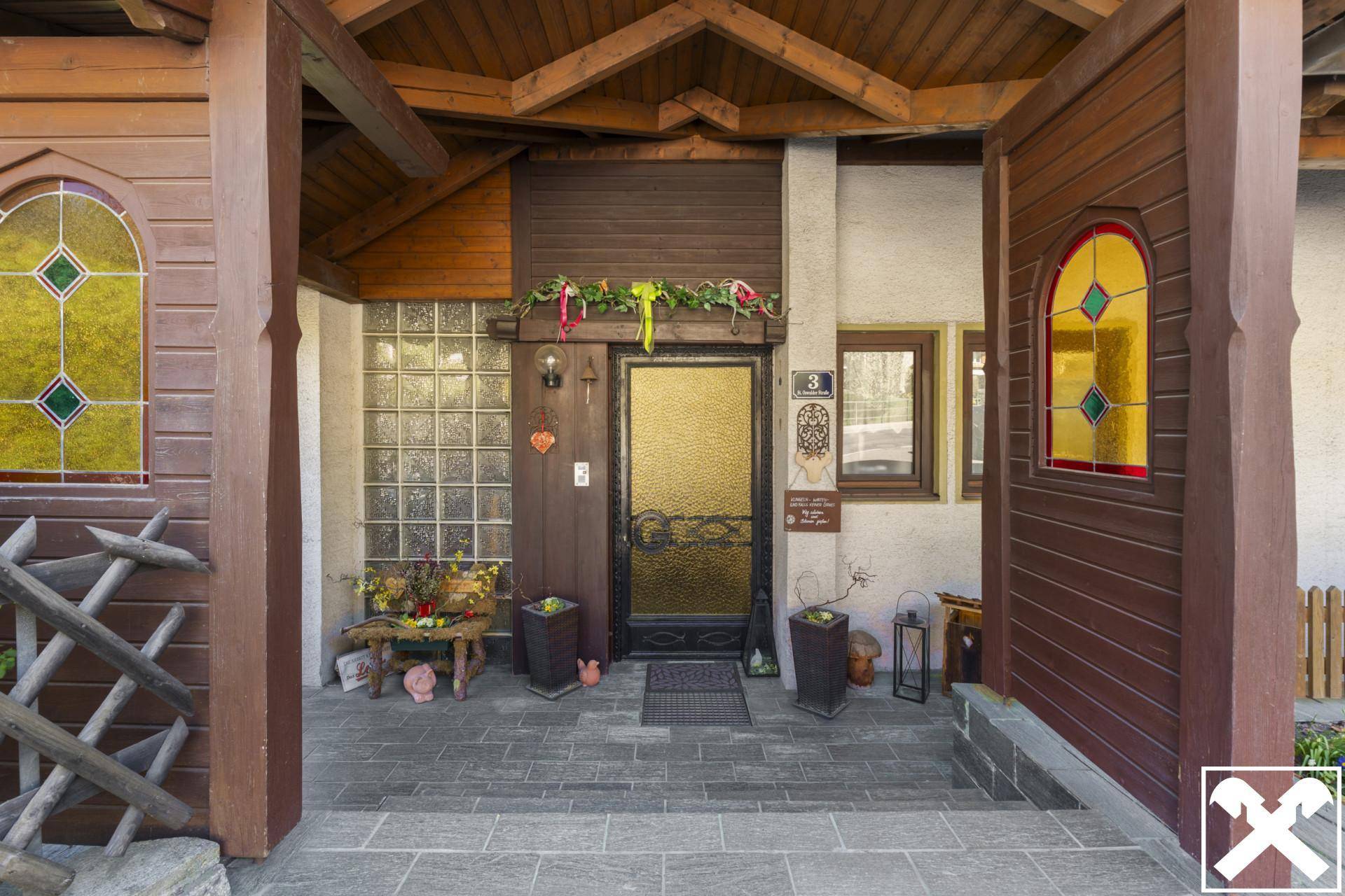 Frontaler Blick auf den überdachten Hauseingang mit Holzelementen und Buntglasfenstern.