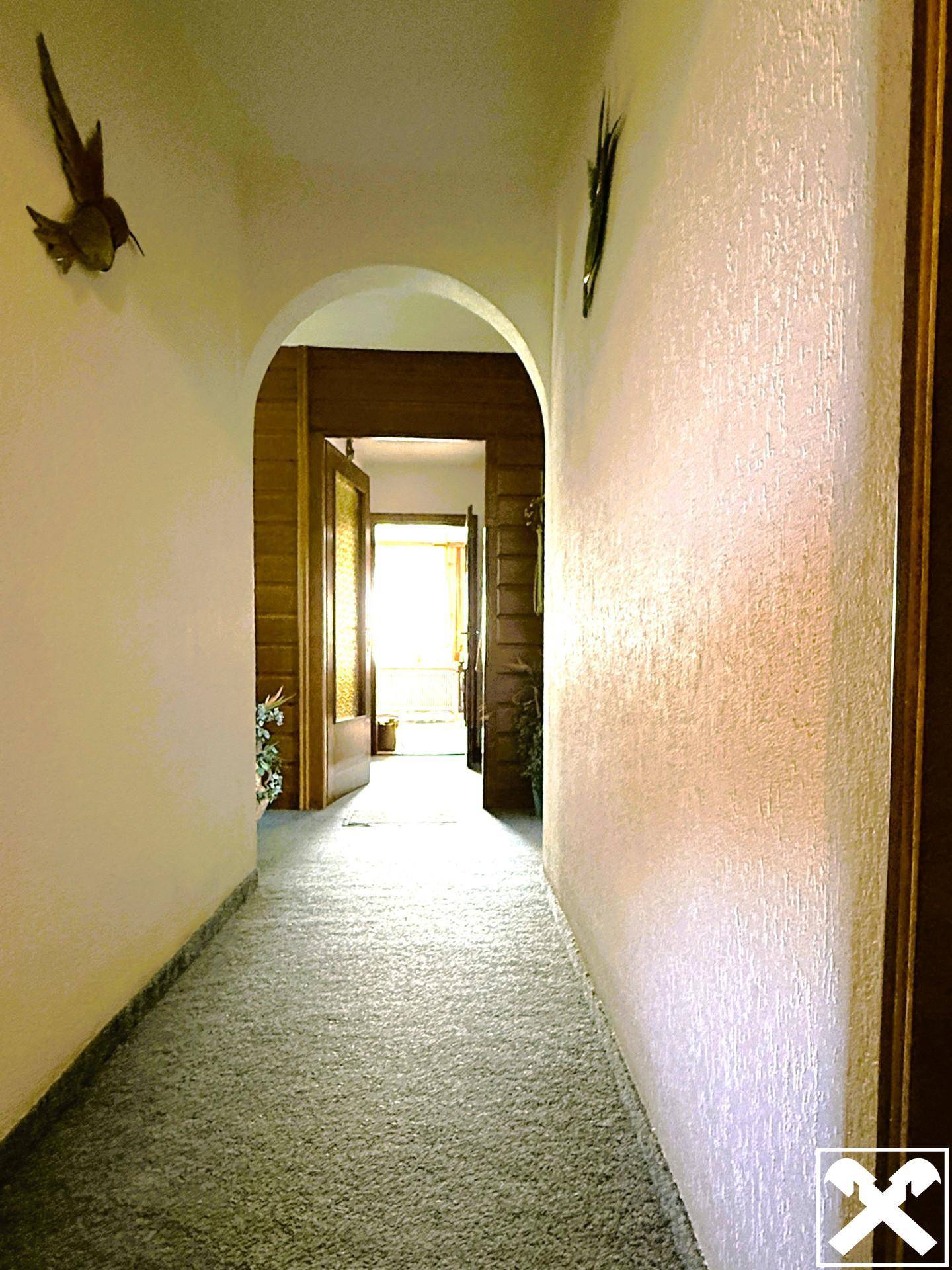 Langer Flur mit Teppichboden und einem Bogen, der zu weiteren Räumen führt.