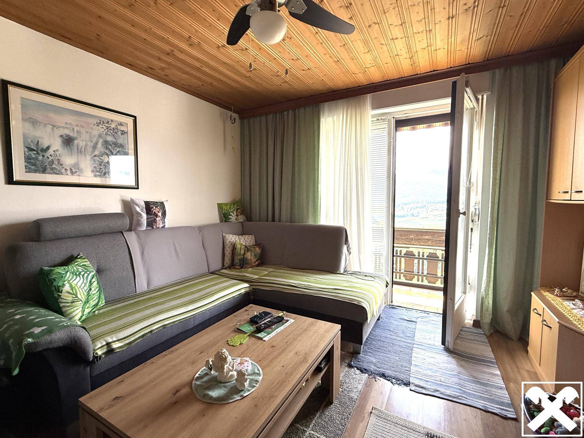 Gemütliches Wohnzimmer mit Ecksofa, Holzbalkendecke und Zugang zum Balkon.