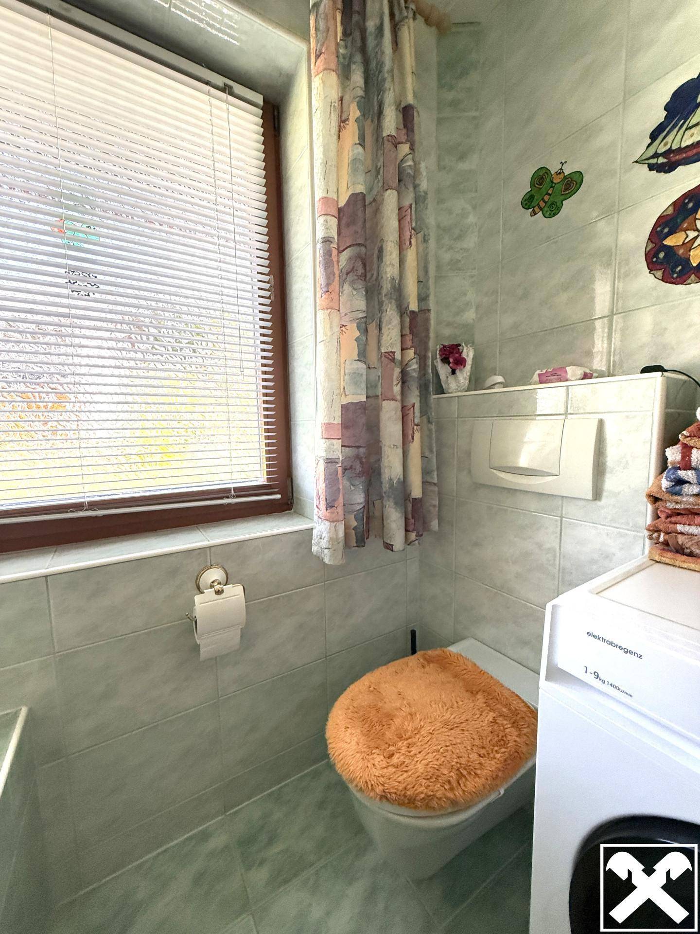 Separate Toilette mit Fenster, Wand-WC und Waschmaschine in hellgrünen Fliesen.