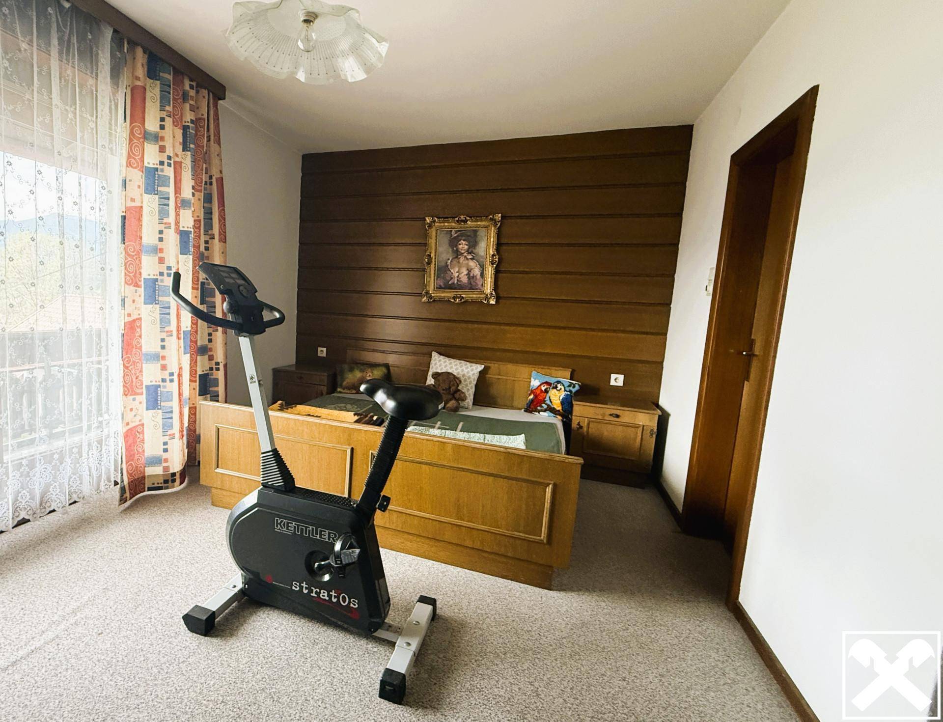 Schlafzimmer mit Holzwandverkleidung, Doppelbett und einem Heimtrainer.