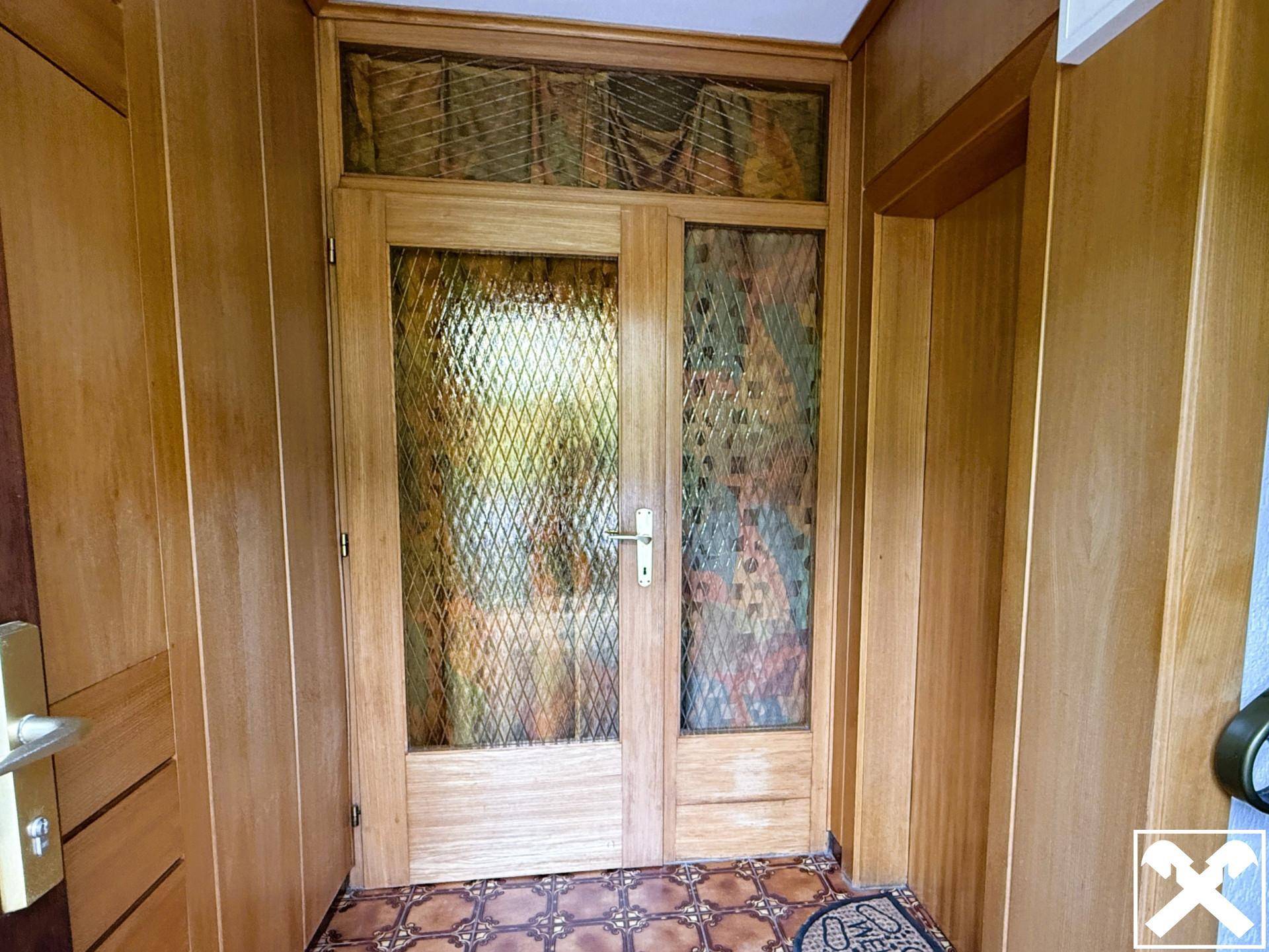 Eingangstür aus Holz mit verzierten Glaseinsätzen und traditionellem Fliesenboden.