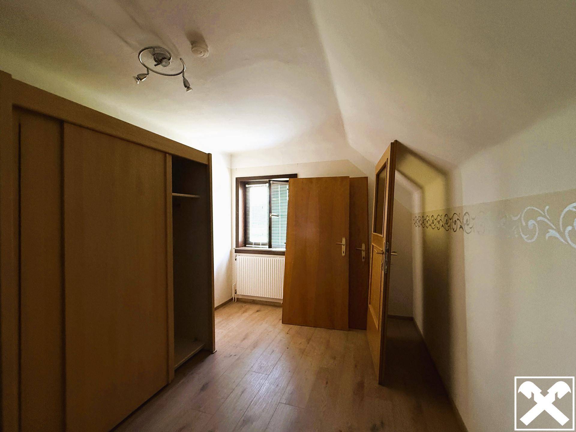 Schlafzimmer mit Holzboden, Einbauschrank und Fenster mit Blick ins Grüne.