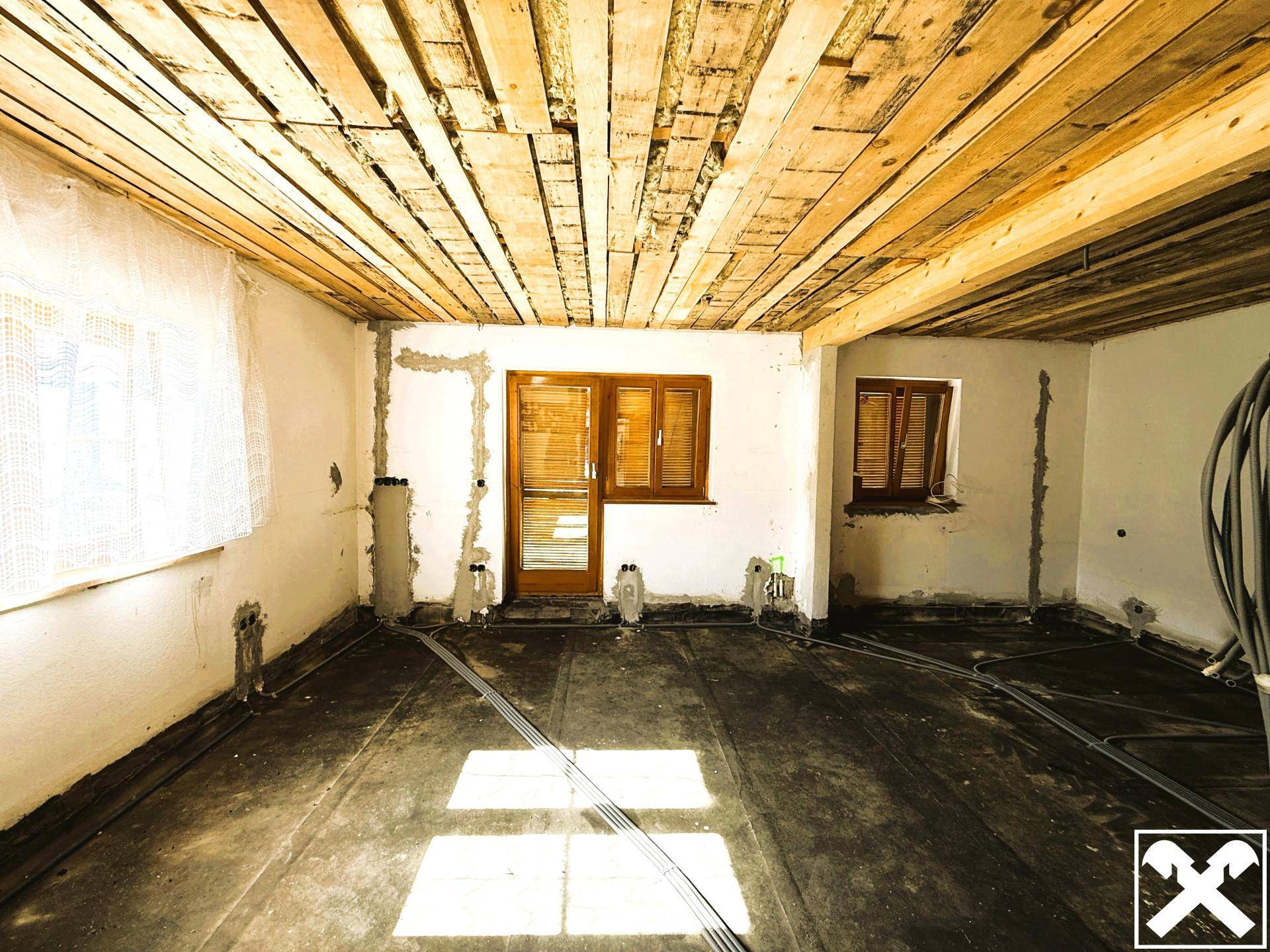 Renovierungsbedürftiger Raum mit Holzdecke und viel natürlichem Licht durch die Fenster.