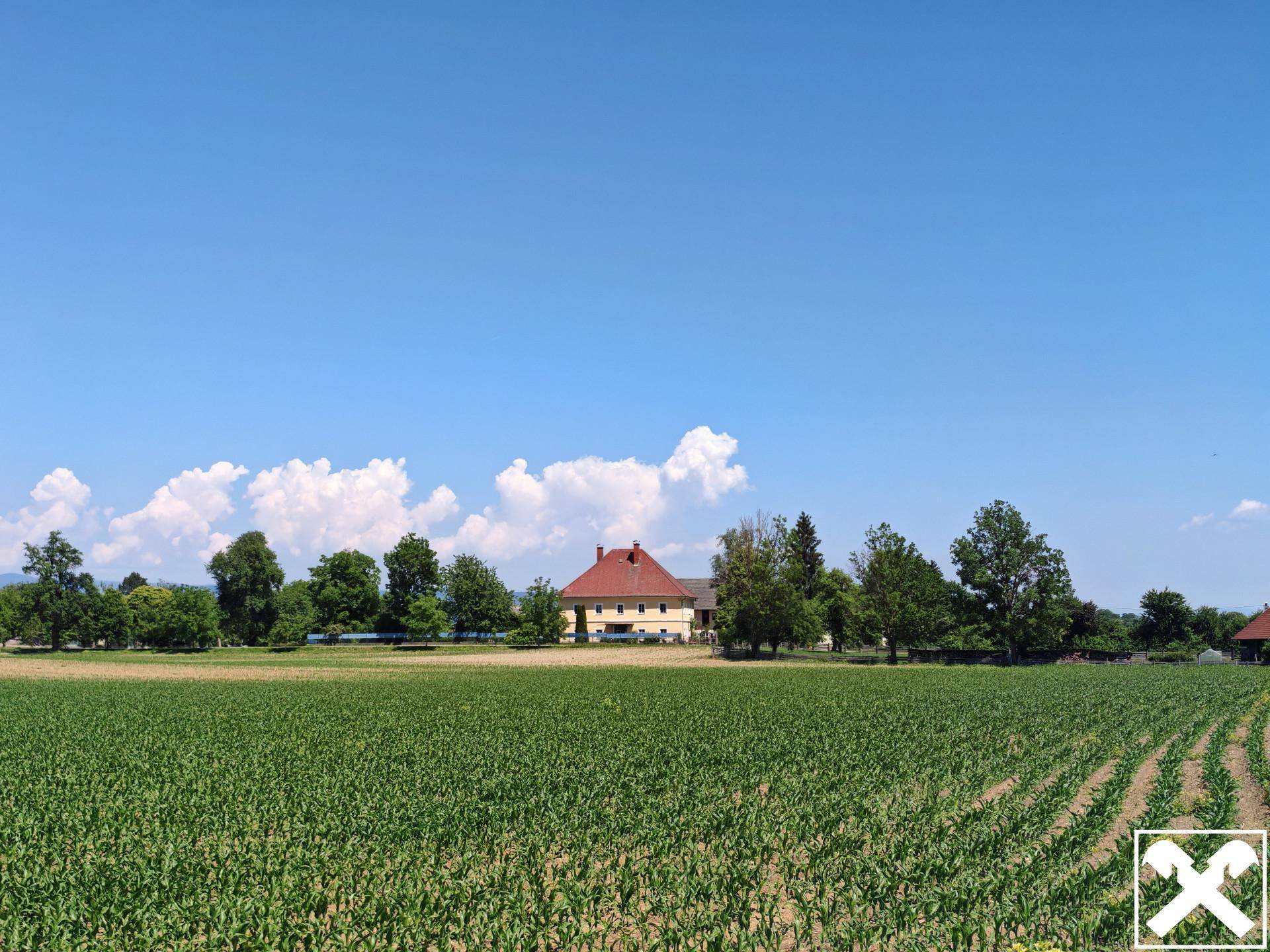 Weitläufiger Blick über ein Feld auf das historische Gebäude und die umliegende Landschaft.