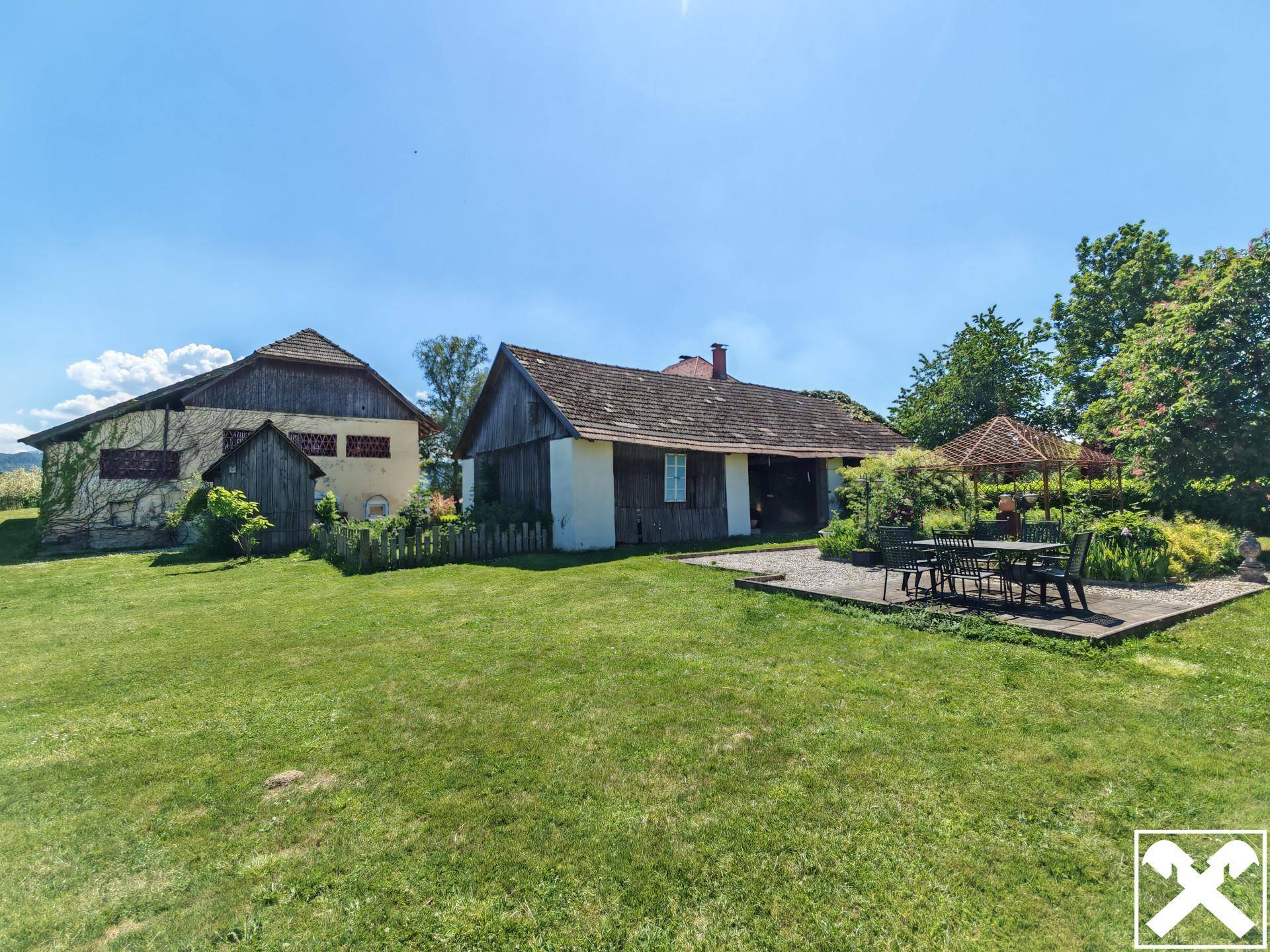 Weitläufiger Gartenbereich mit Rasenfläche, Holzterrasse und Gartenmöbeln zwischen den Gebäuden.