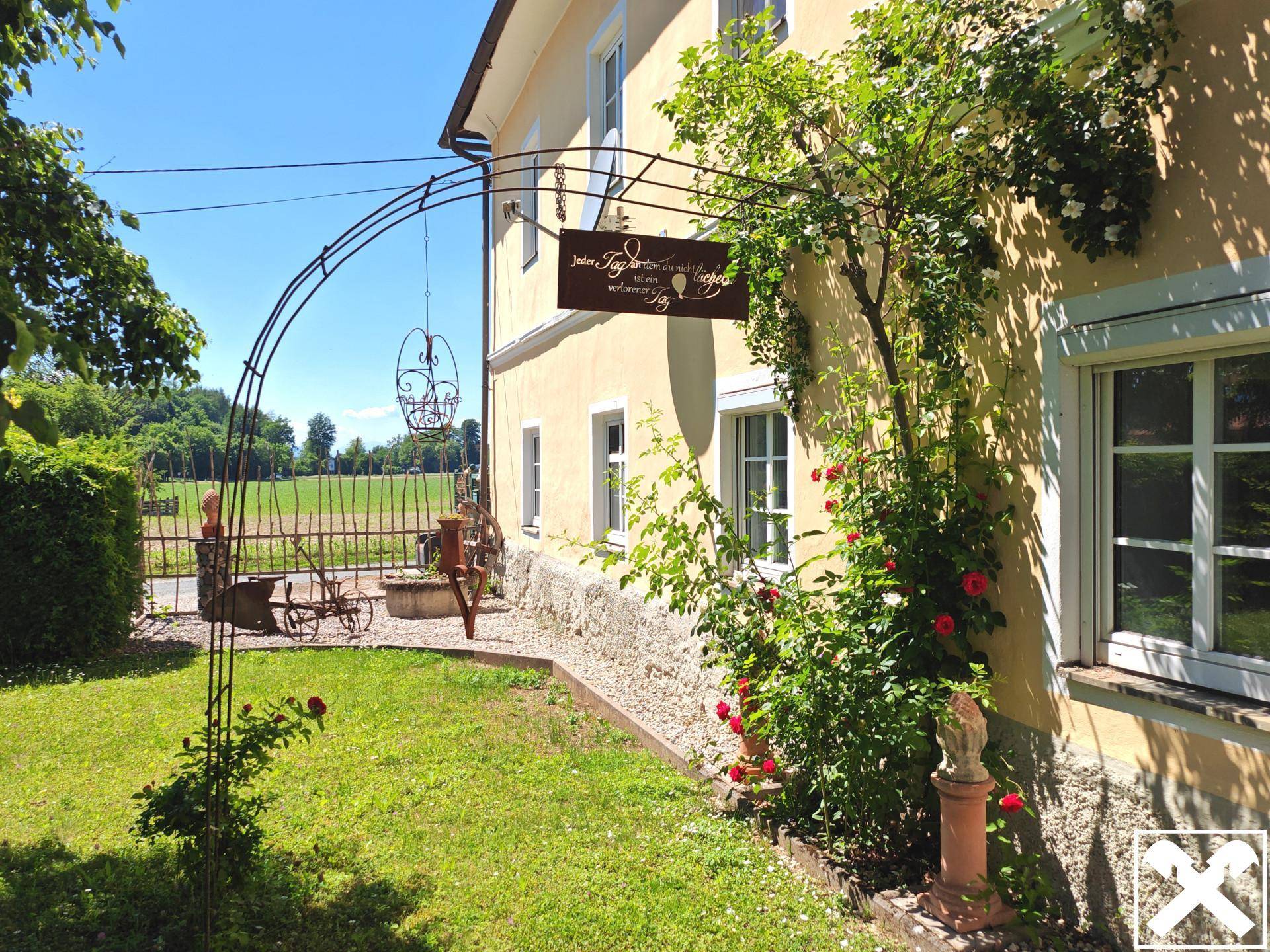 Seitlicher Blick auf das Haus mit einem Rosenbogen und einem kleinen, gepflegten Gartenbereich.