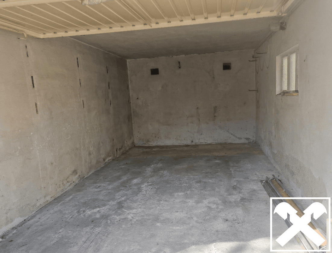 Leere Garage mit Betonboden und einem kleinen Fenster für Tageslicht.