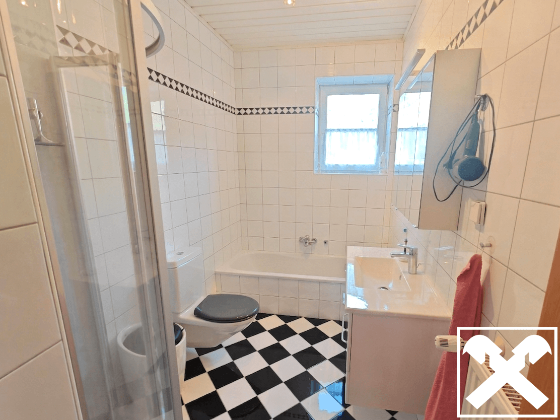 Badezimmer mit Badewanne, Dusche, WC und auffälligem schwarz-weiß kariertem Fliesenboden.