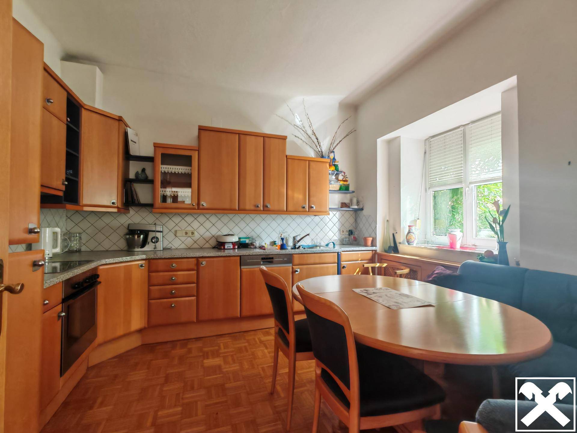 Gemütliche Wohnküche mit Holzeinbauten, Essbereich und Blick ins Grüne durch das Fenster.
