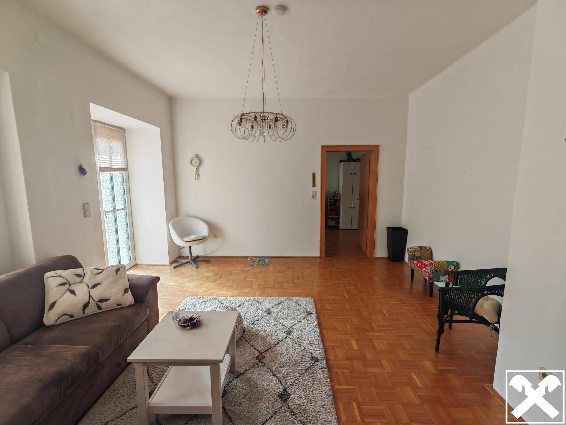 Helles Wohnzimmer mit Parkettboden, bequemer Couch und modernem Kronleuchter.