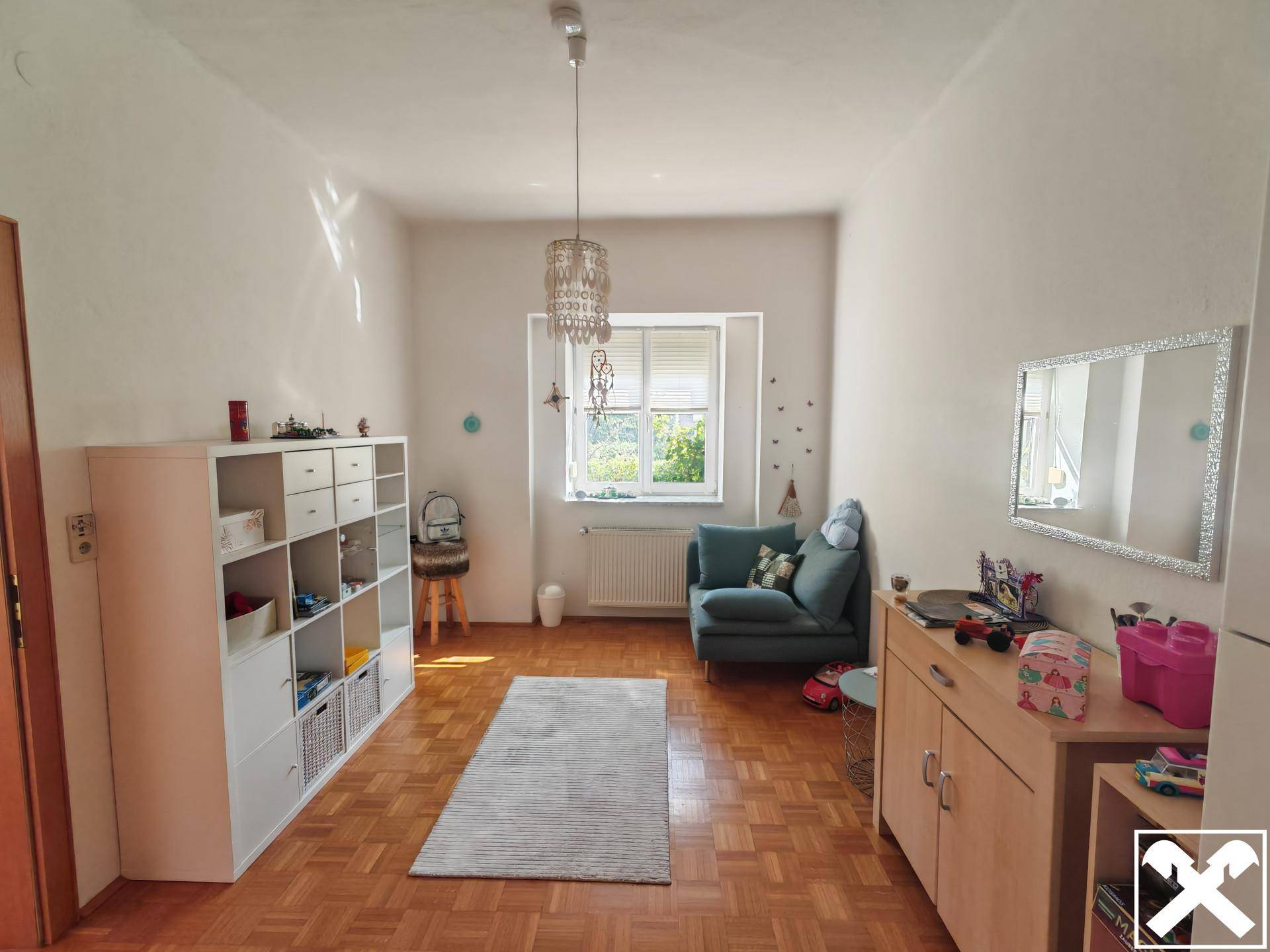 Freundliches Zimmer mit Parkettboden, Fenster und praktischen Regalen für Stauraum.