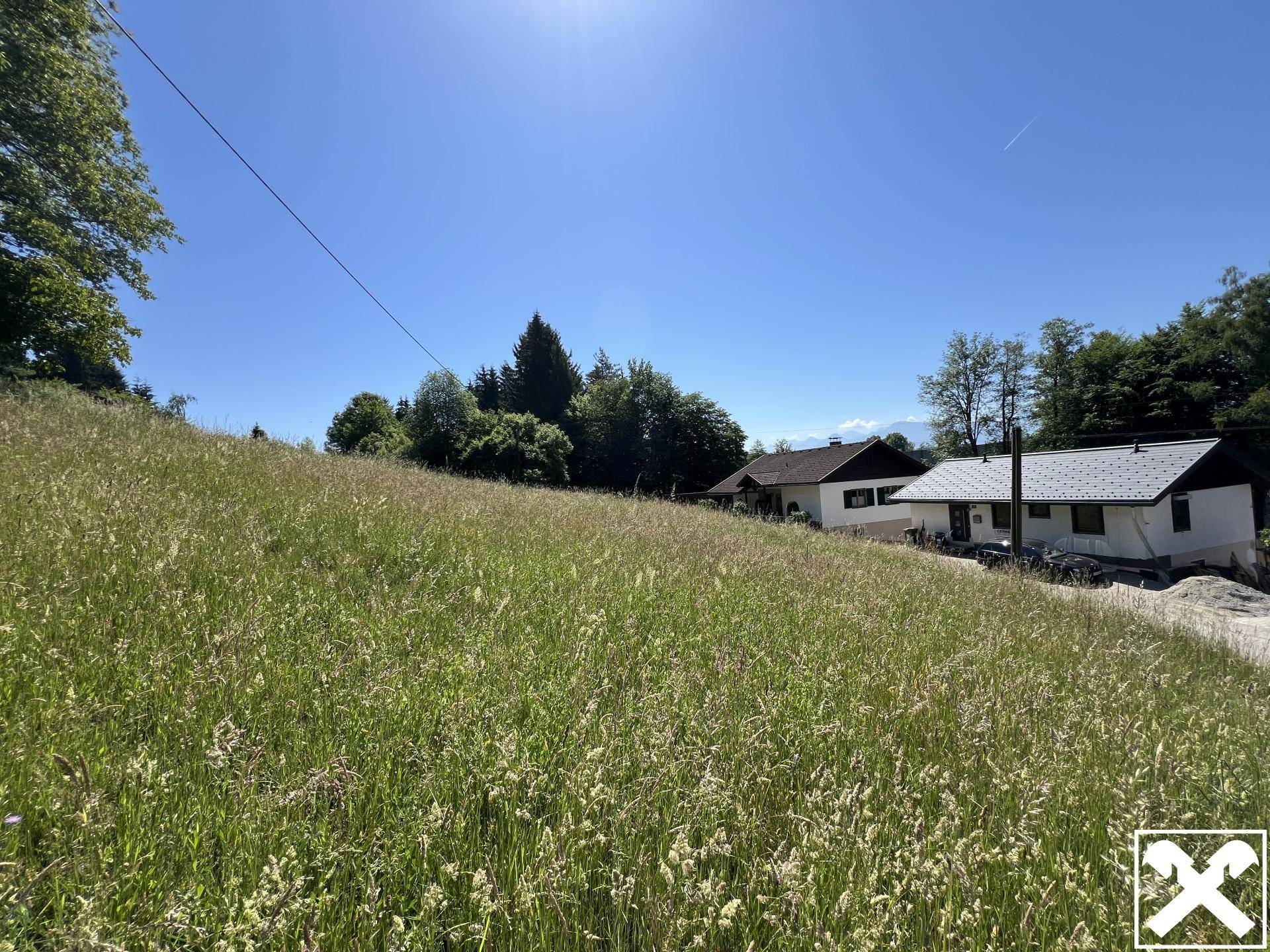 Weitläufige grüne Wiese mit Häusern im Hintergrund unter strahlend blauem Himmel.