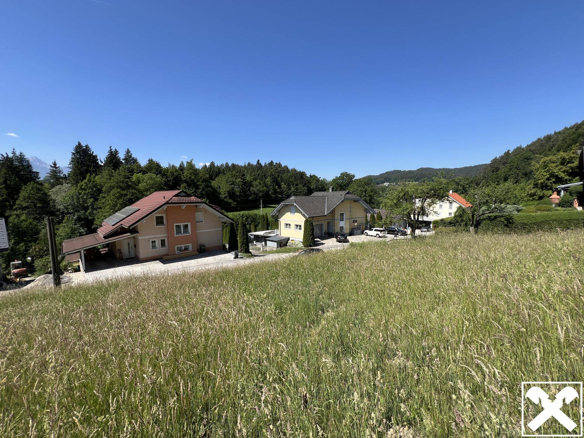 Offene grüne Landschaft mit Wohnhäusern und üppiger Vegetation unter klarem Himmel.