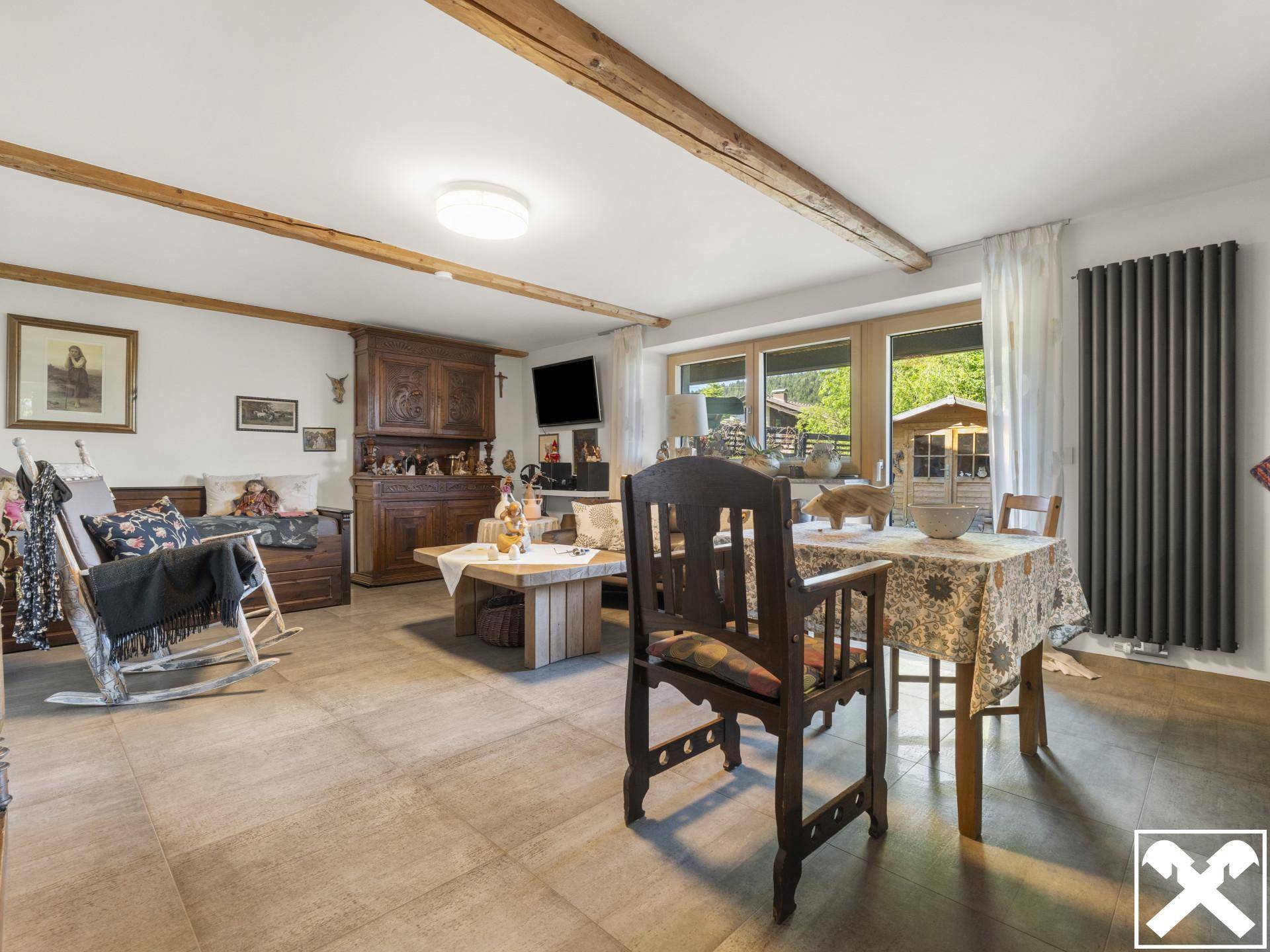 Rustikales Wohnzimmer mit Holzbalken, traditionellen Möbeln und großem Fenster mit Blick ins Grüne.