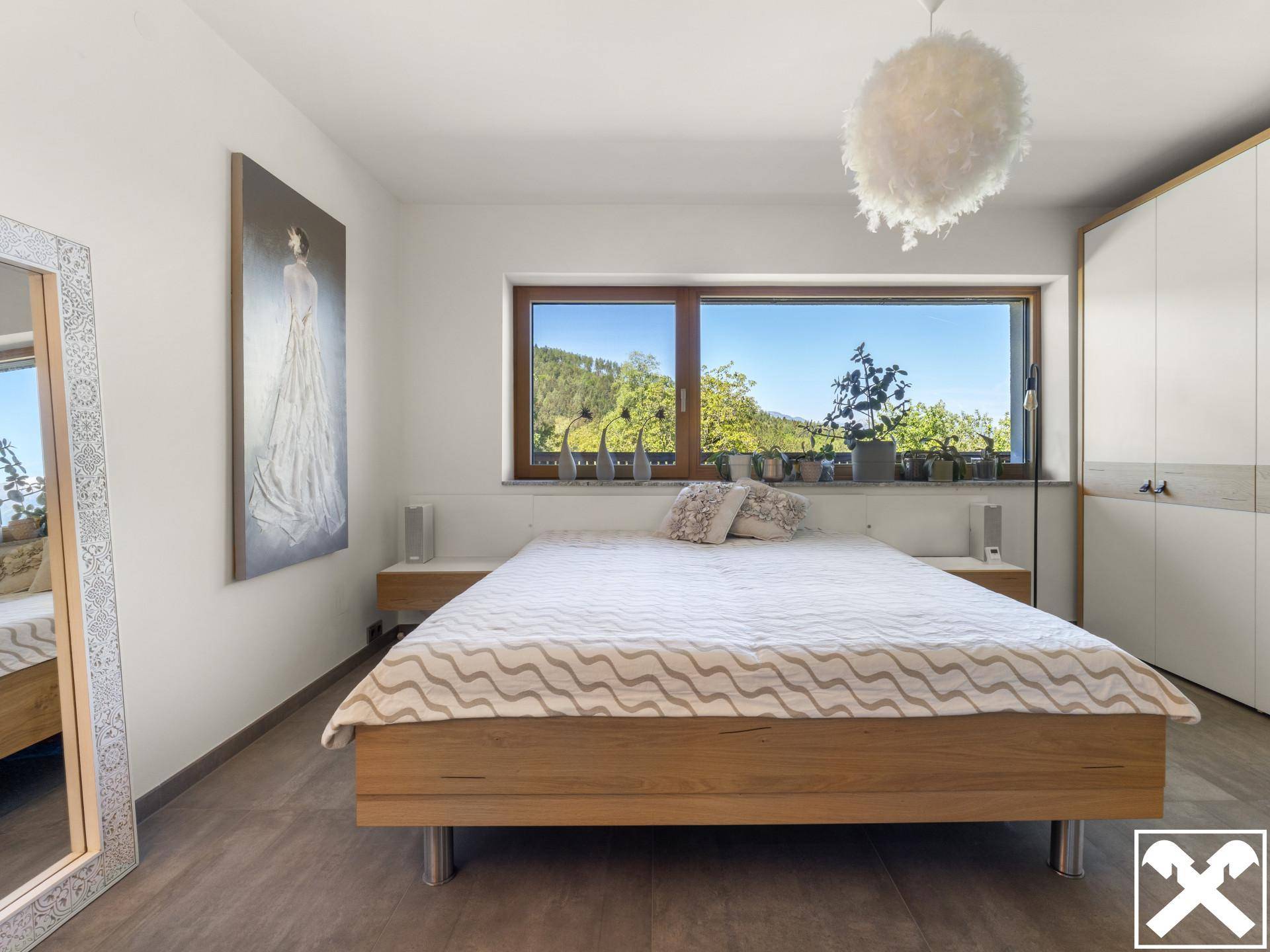 Helles Schlafzimmer mit Holzbett, Einbauschränken und großem Fenster mit Blick ins Grüne.