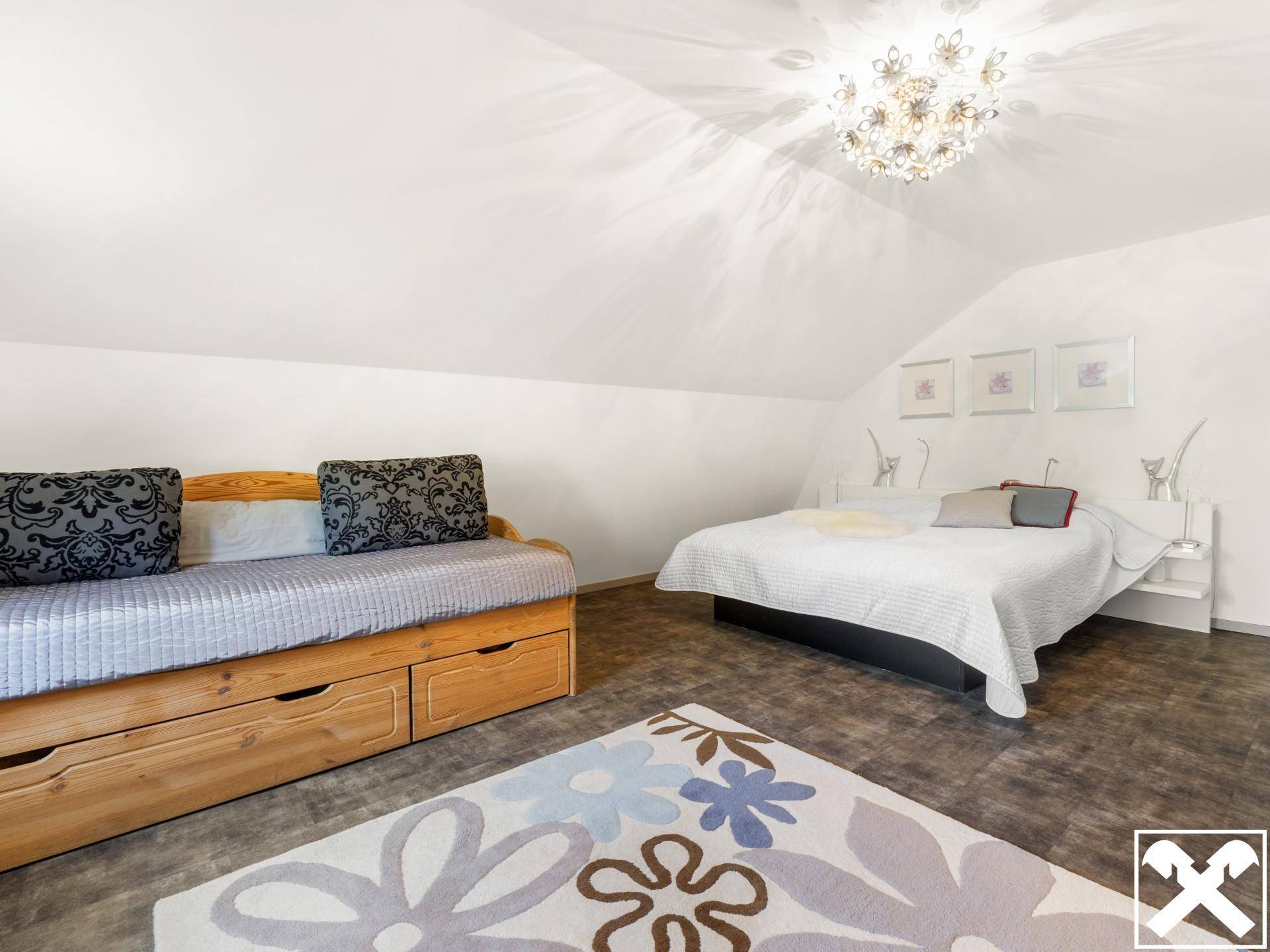 Gemütliches Schlafzimmer im Dachgeschoss mit Dachschrägen, Tagesbett und floralem Teppich.