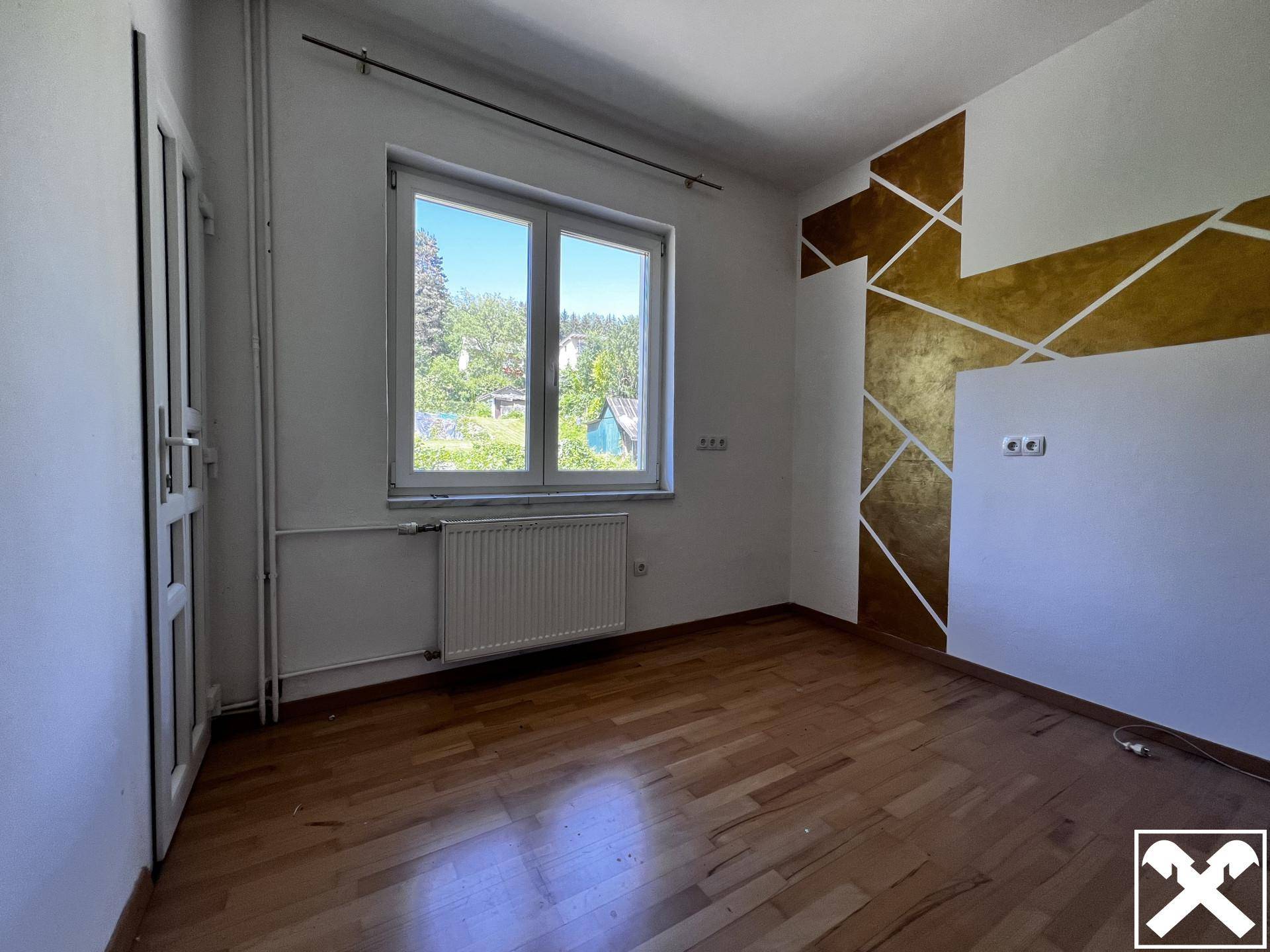 Helles Zimmer mit Parkettboden, Heizkörper und einer dekorativen Gold-Wandgestaltung.