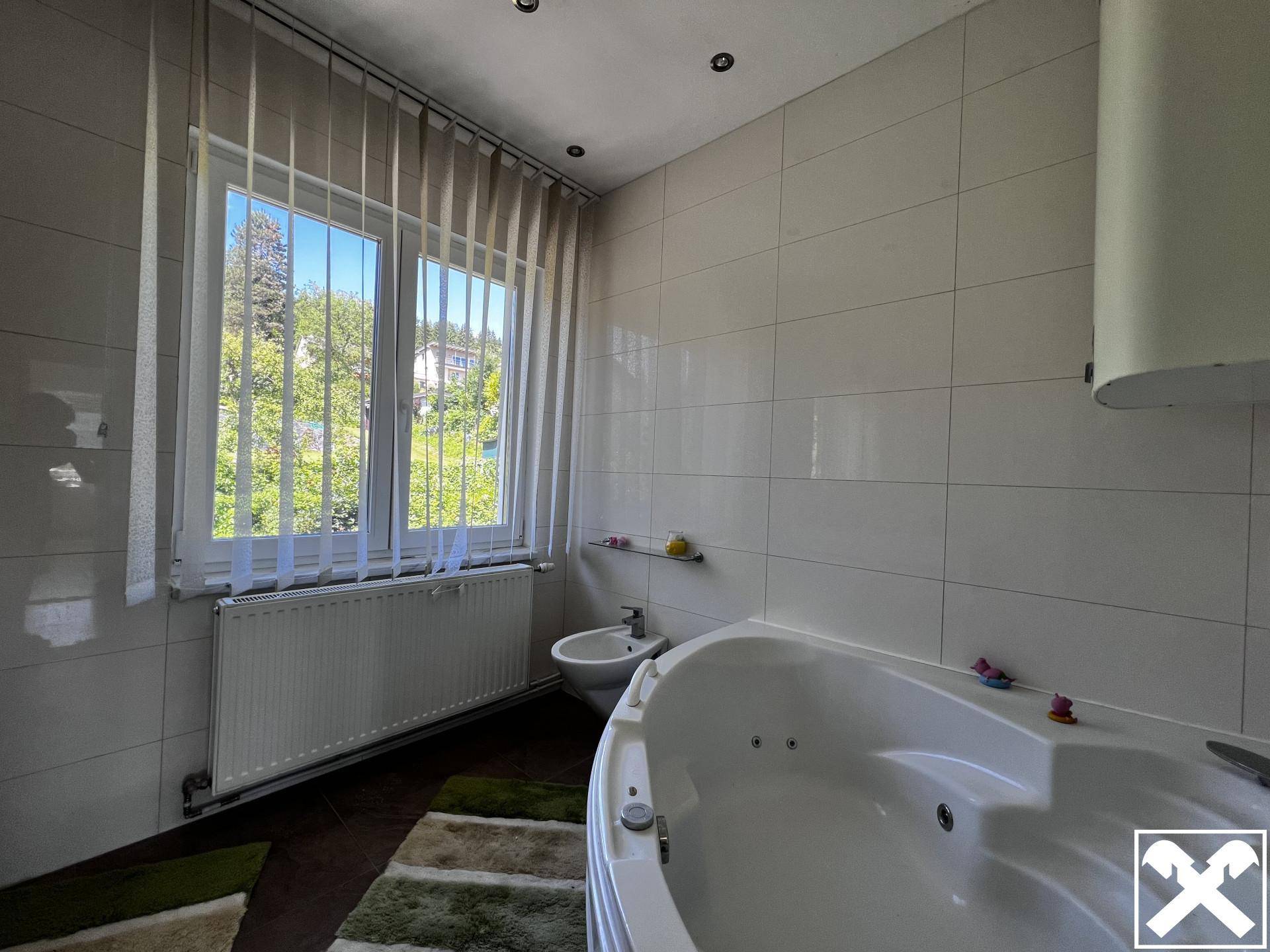 Gefliestes Badezimmer mit Whirlpool-Badewanne, Bidet und großem Fenster mit Blick ins Grüne.