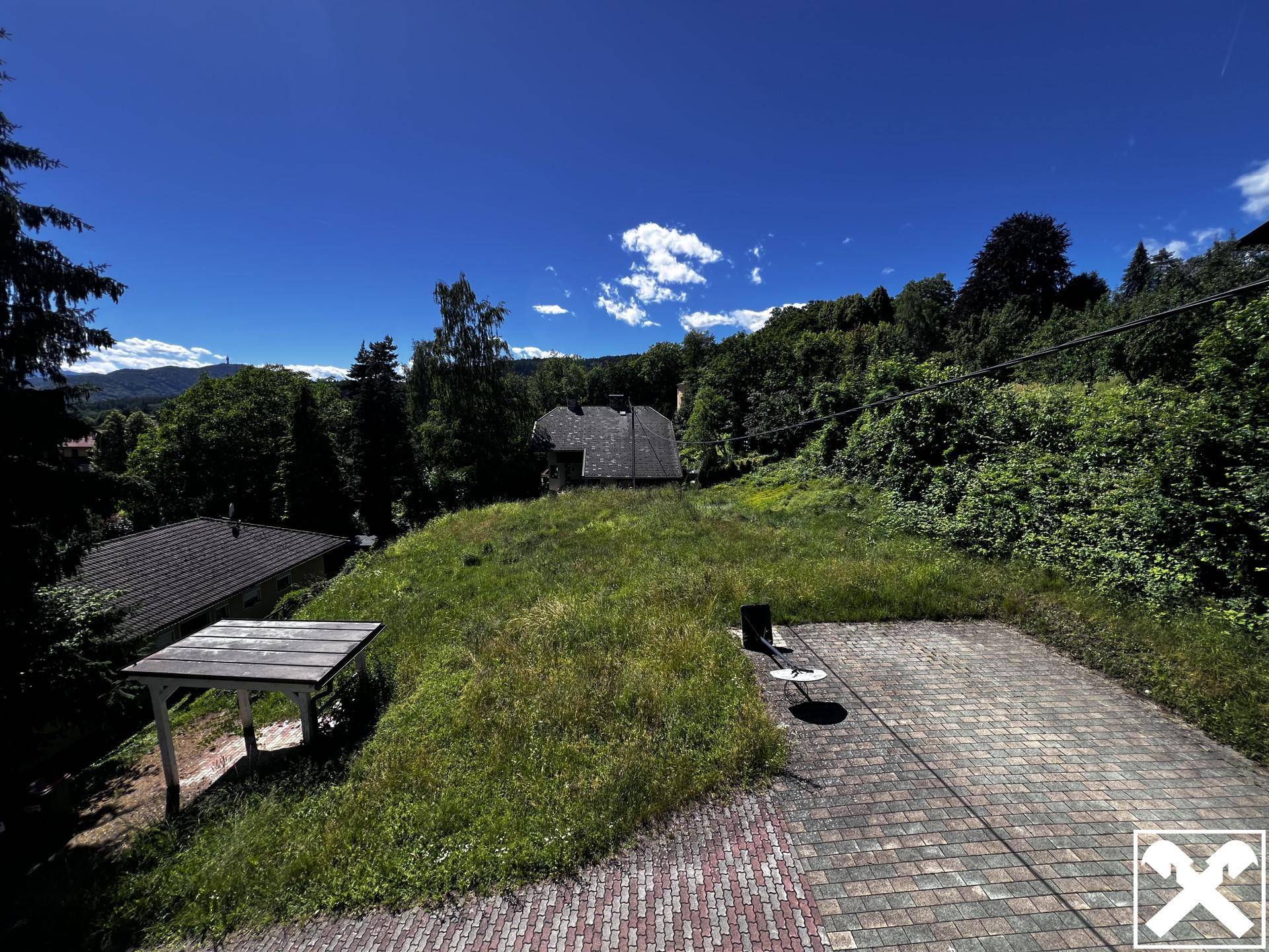 Weitläufiges Grundstück mit Rasenfläche, gepflastertem Bereich und Fernblick auf die umliegende Landschaft.