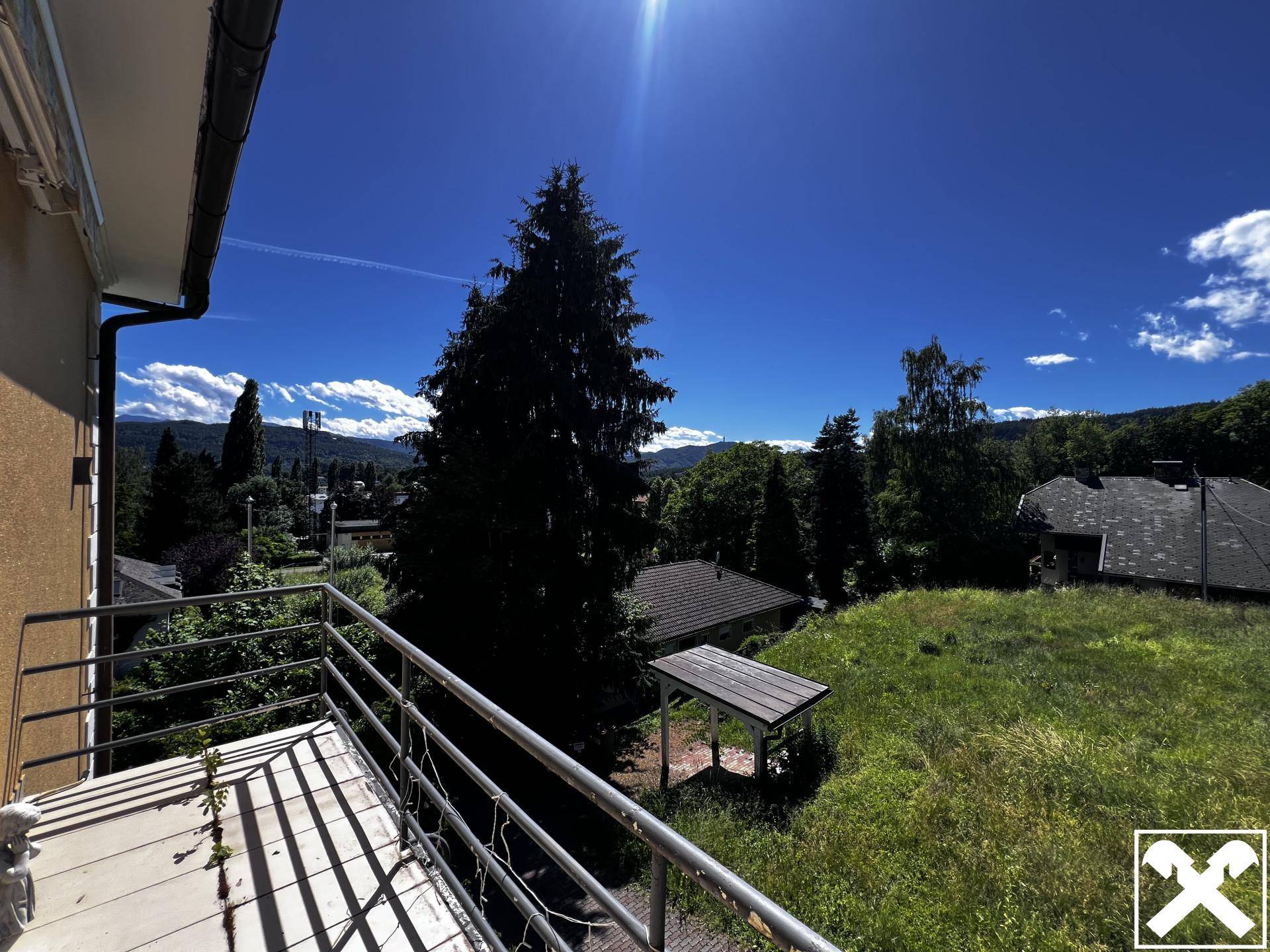 Balkon mit Metallgeländer bietet einen weiten Blick über die grüne Landschaft und Dächer.
