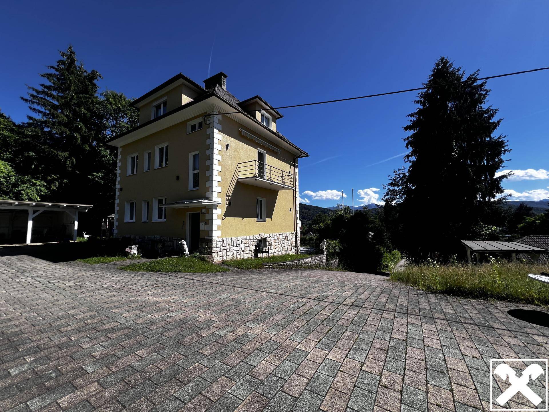 Ansicht des Hauses mit gepflasterter Zufahrt und umgebender Natur unter strahlendem Sonnenschein.