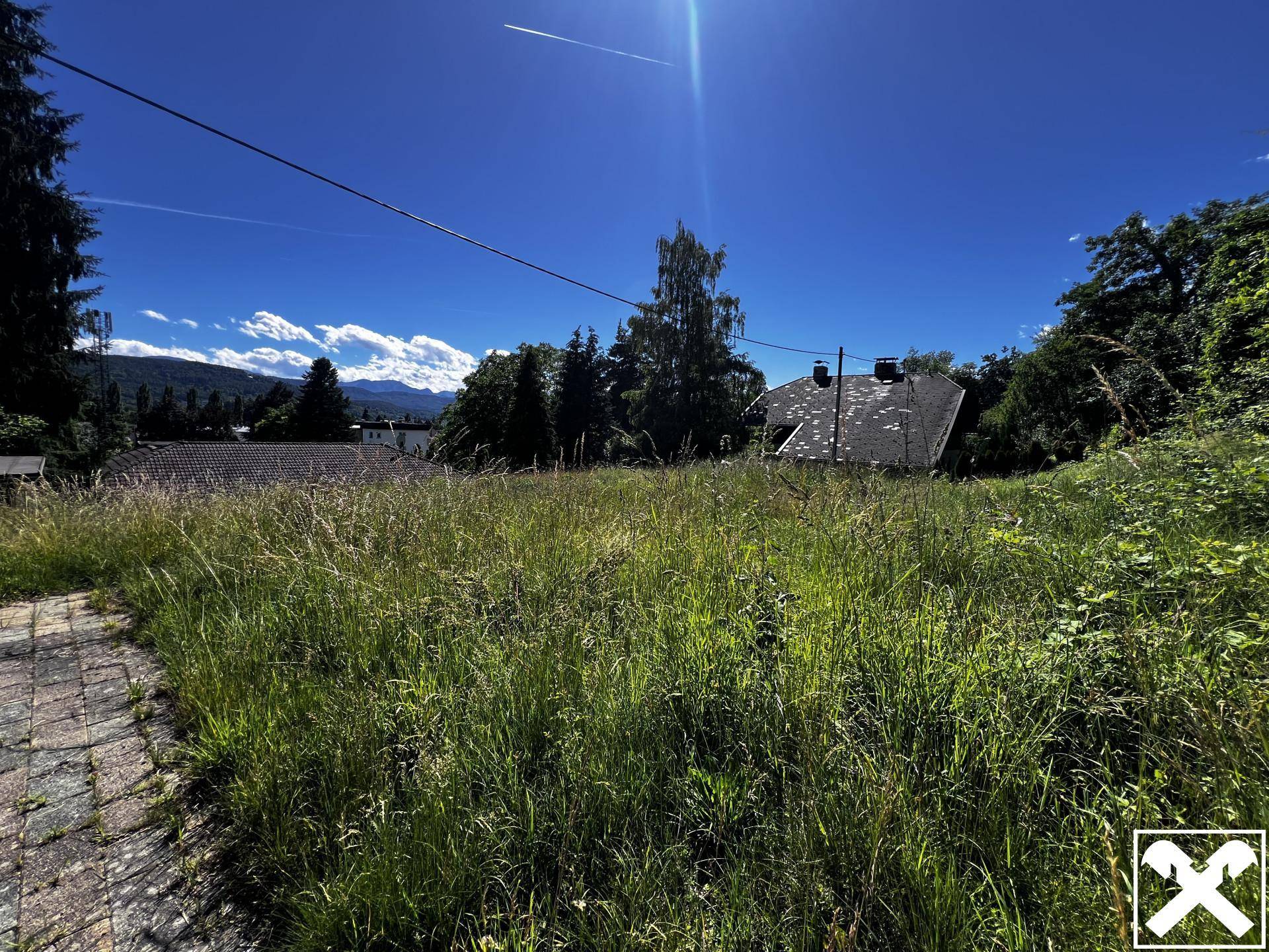 Weitläufige, ungemähte Wiesenfläche des Grundstücks unter strahlendem Sonnenschein mit Fernblick.