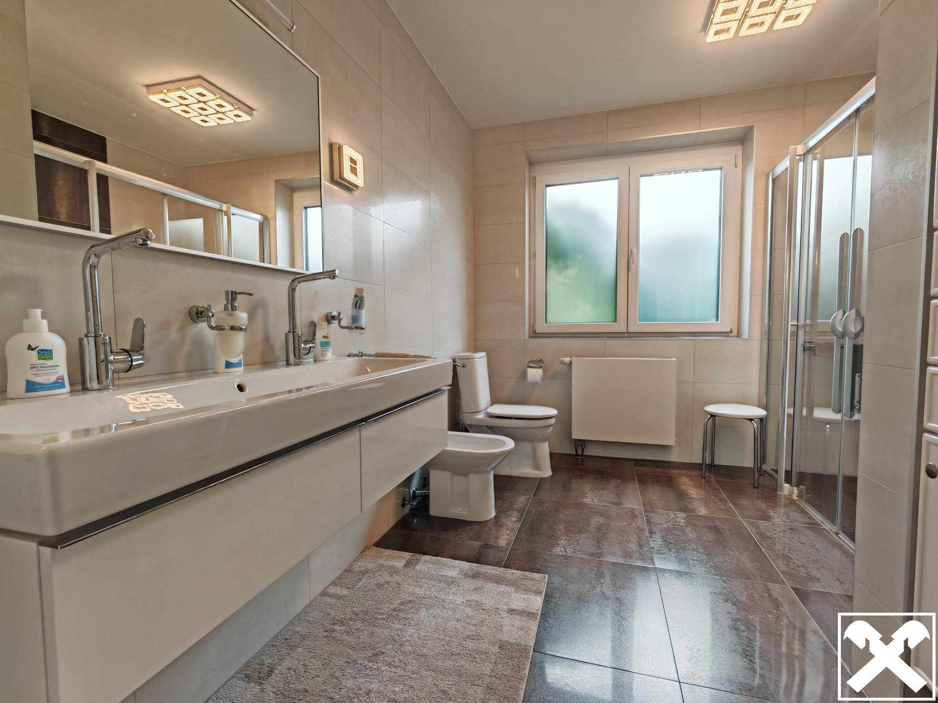 Modernes Badezimmer mit Doppelwaschbecken, Dusche, Bidet und großformatigen Fliesen.