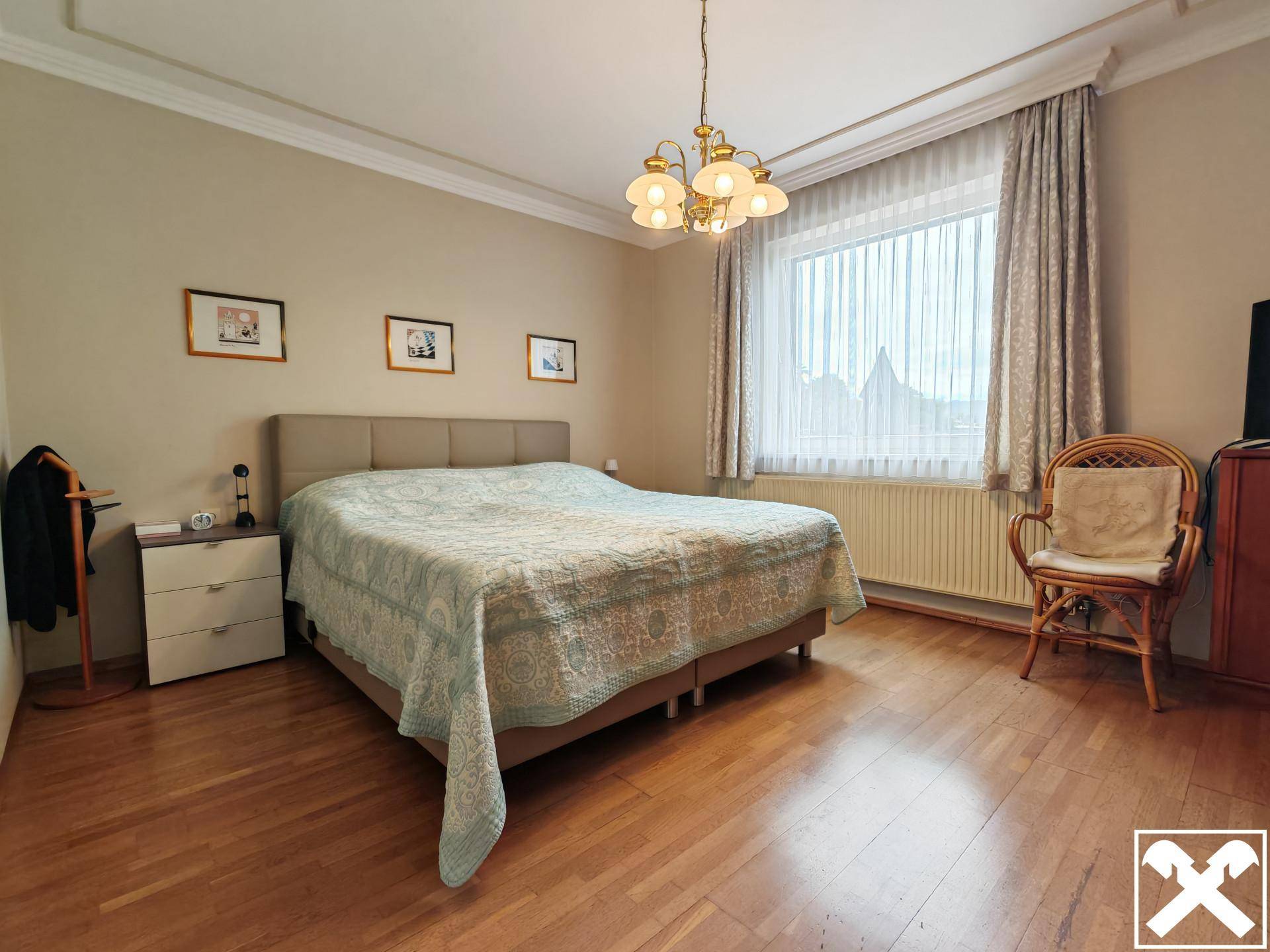 Helles Schlafzimmer mit Doppelbett, Holzparkett und einem großen Fenster mit Vorhängen.