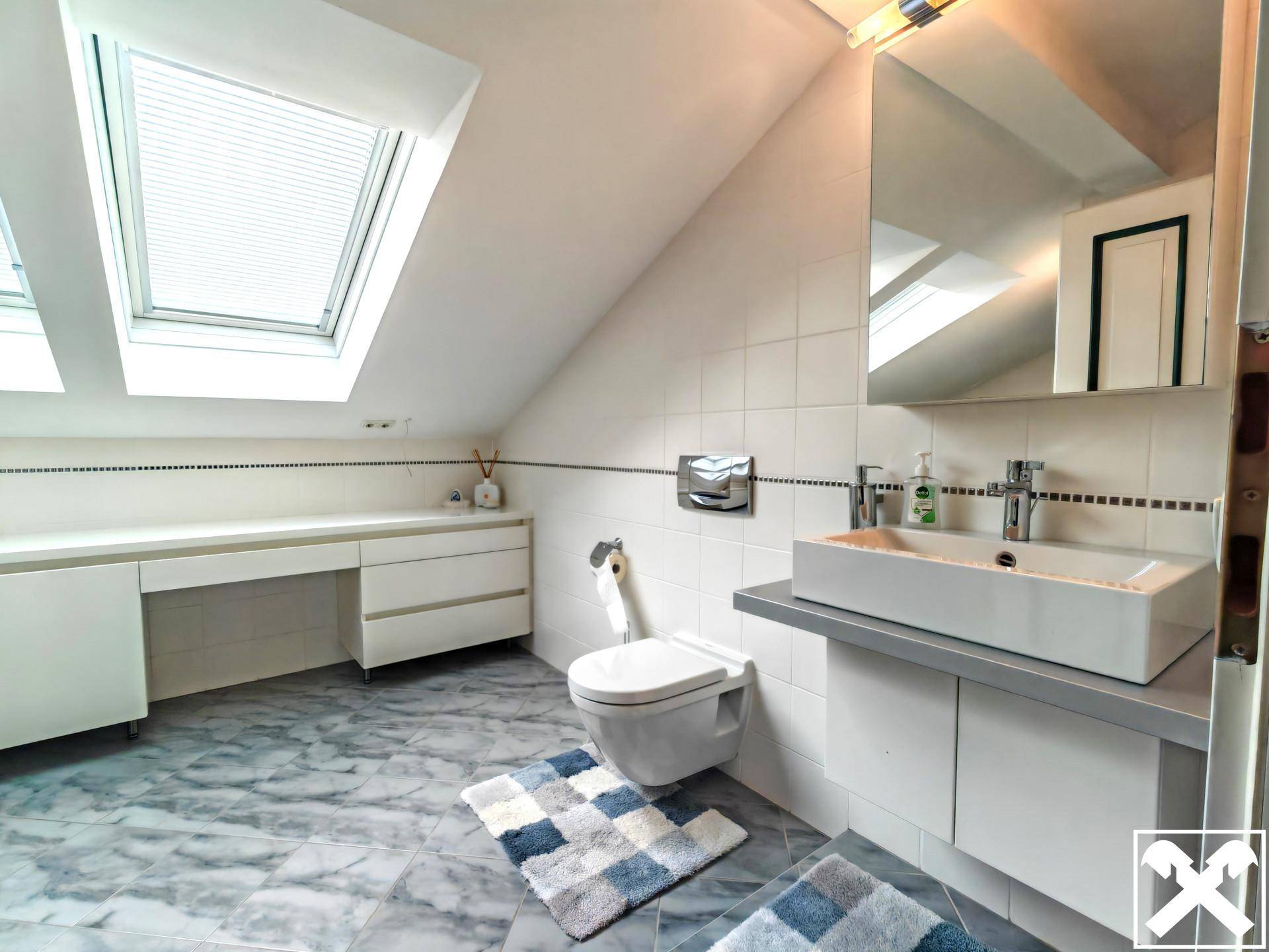 Modernes Badezimmer im Dachgeschoss mit Waschtisch, Toilette und Dachfenstern.