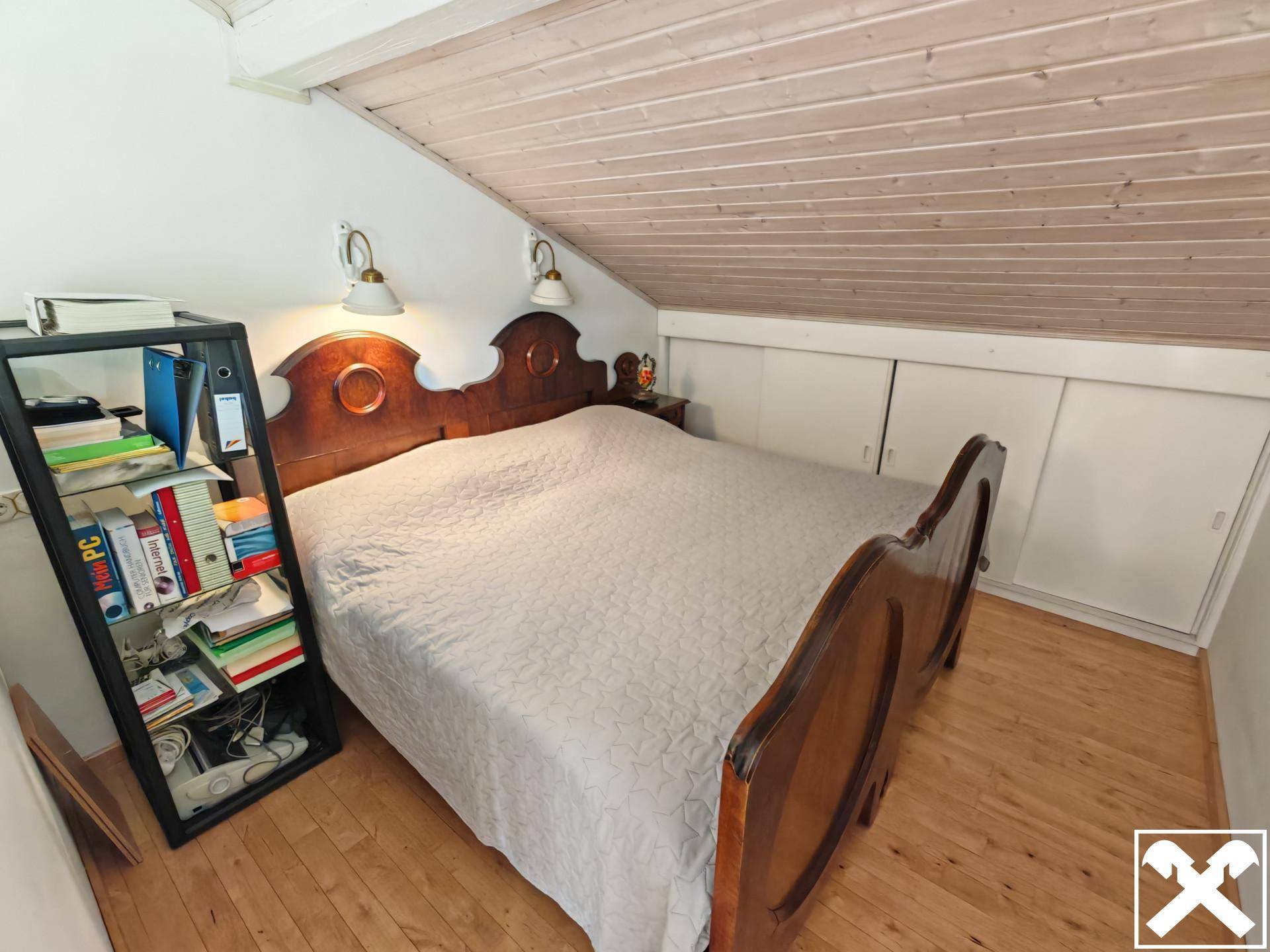Schlafzimmer im Dachgeschoss mit Holzbett, Holzdecke und integrierten Stauschränken.