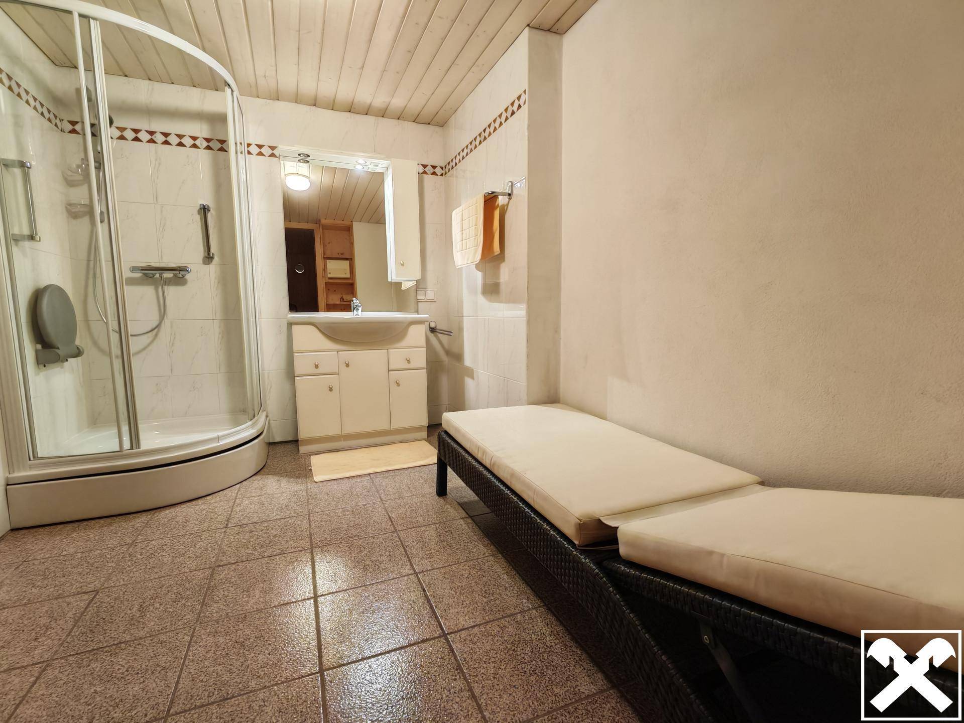 Geräumiges Badezimmer mit Duschkabine, Waschbecken und Liegen für eine entspannte Atmosphäre.