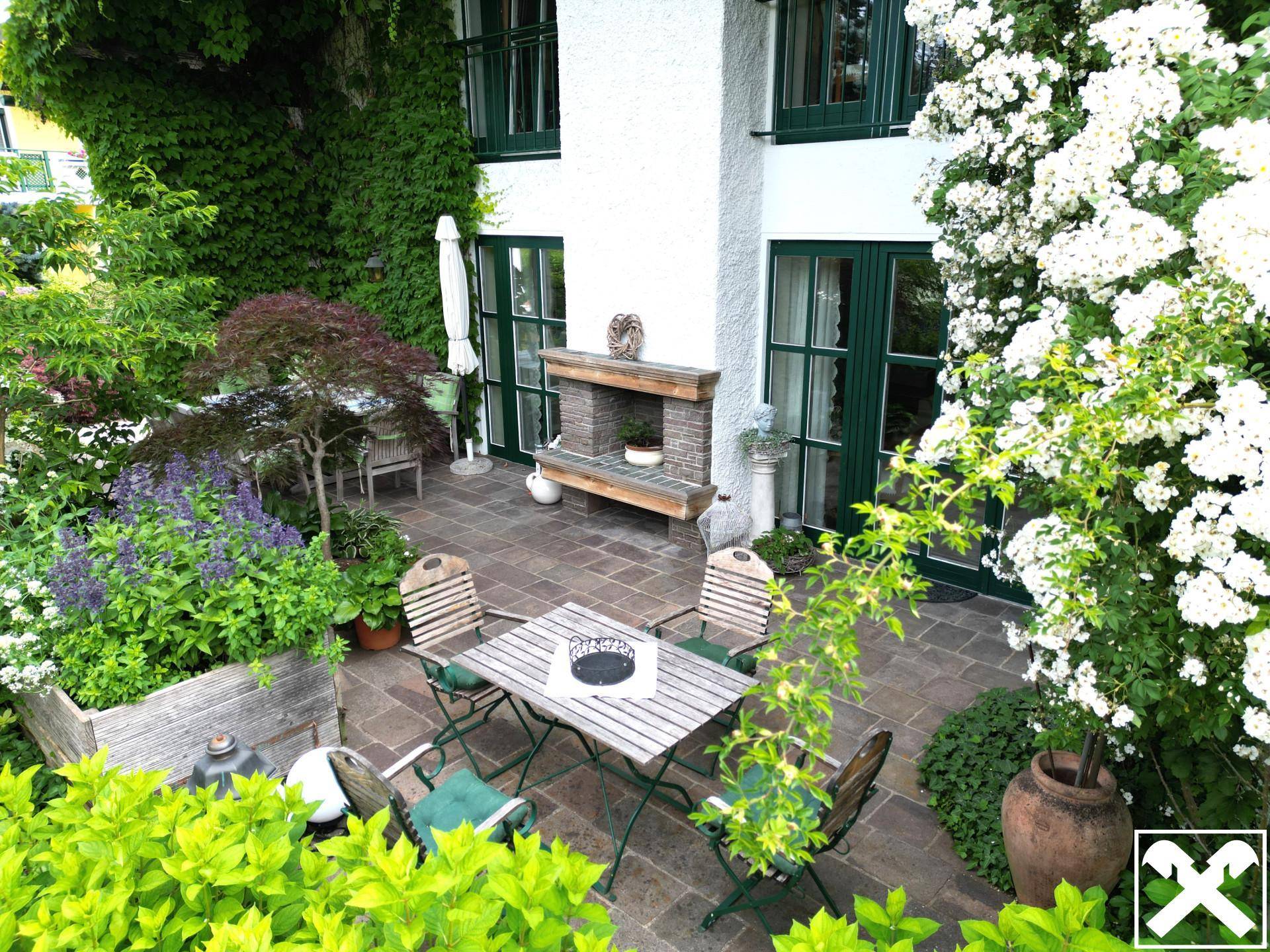 Charmante Terrasse mit Gartenmöbeln, umgeben von üppiger Vegetation und Kletterpflanzen.